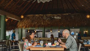 A restaurant with wooden tables and chairs, a thatched roof, and hanging lights.