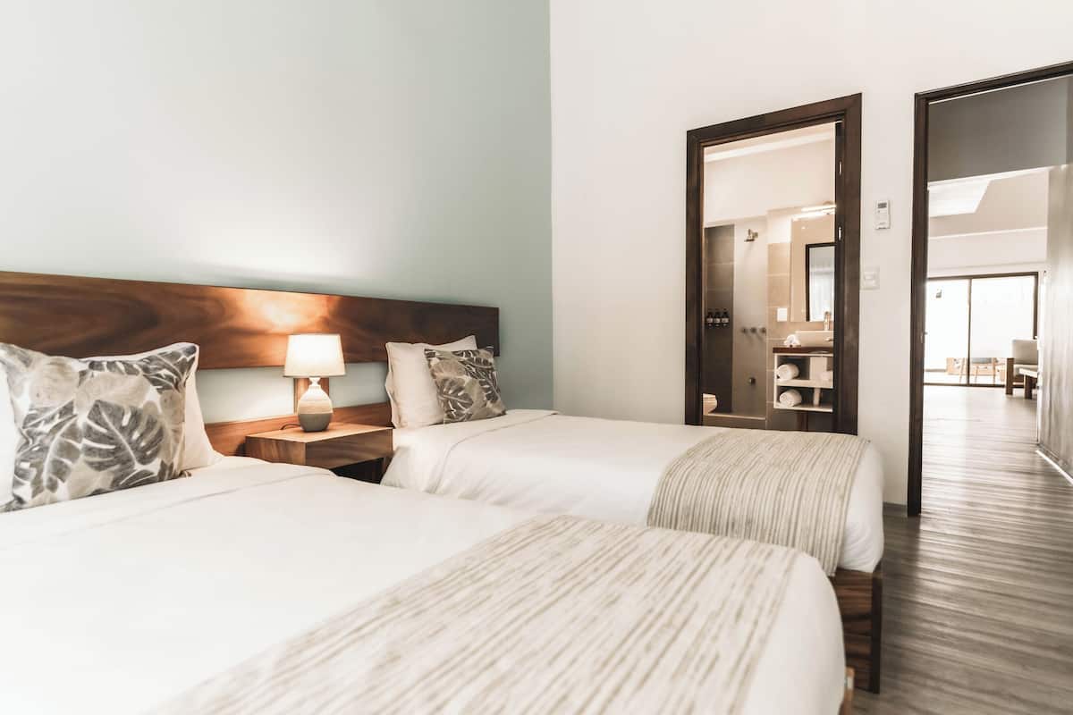 Une chambre d’hôtel avec deux lits, une tête de lit en bois, une table de chevet avec une lampe et un miroir.