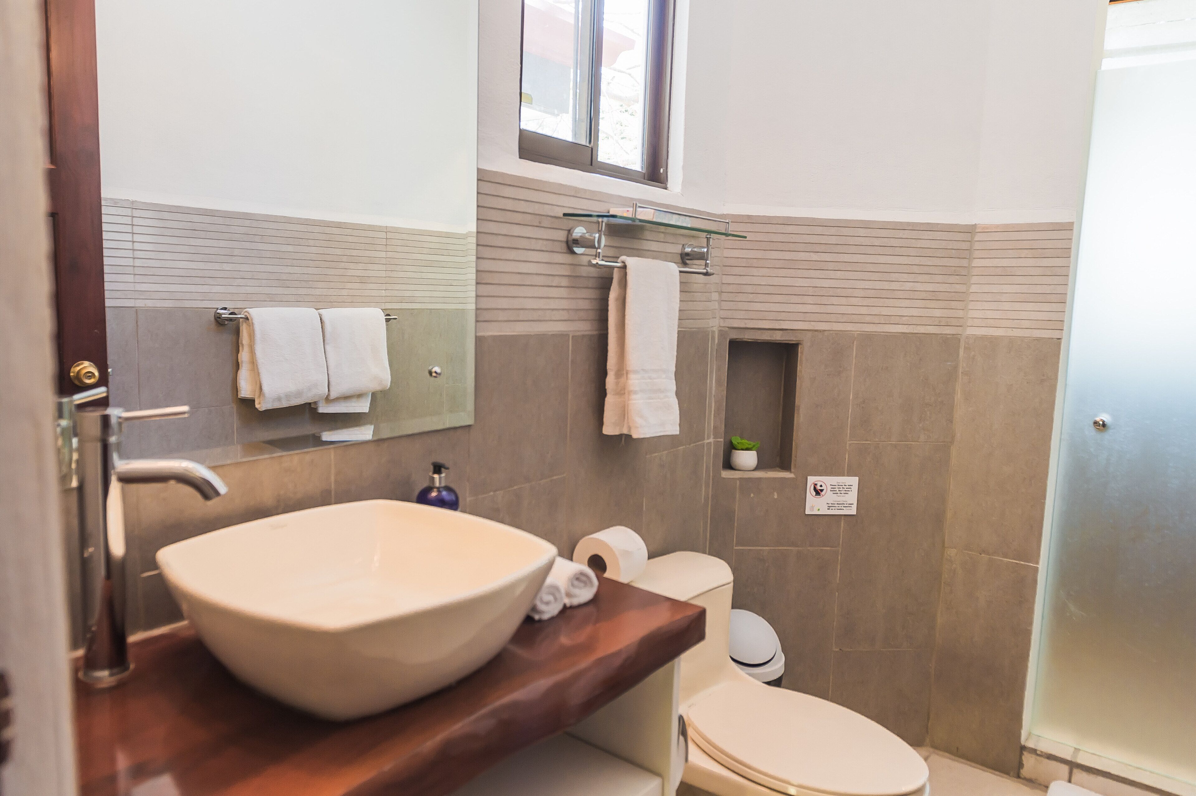 A modern bathroom with a large vessel sink, a mirror, a towel rack, a toilet, and a glass-enclosed shower.