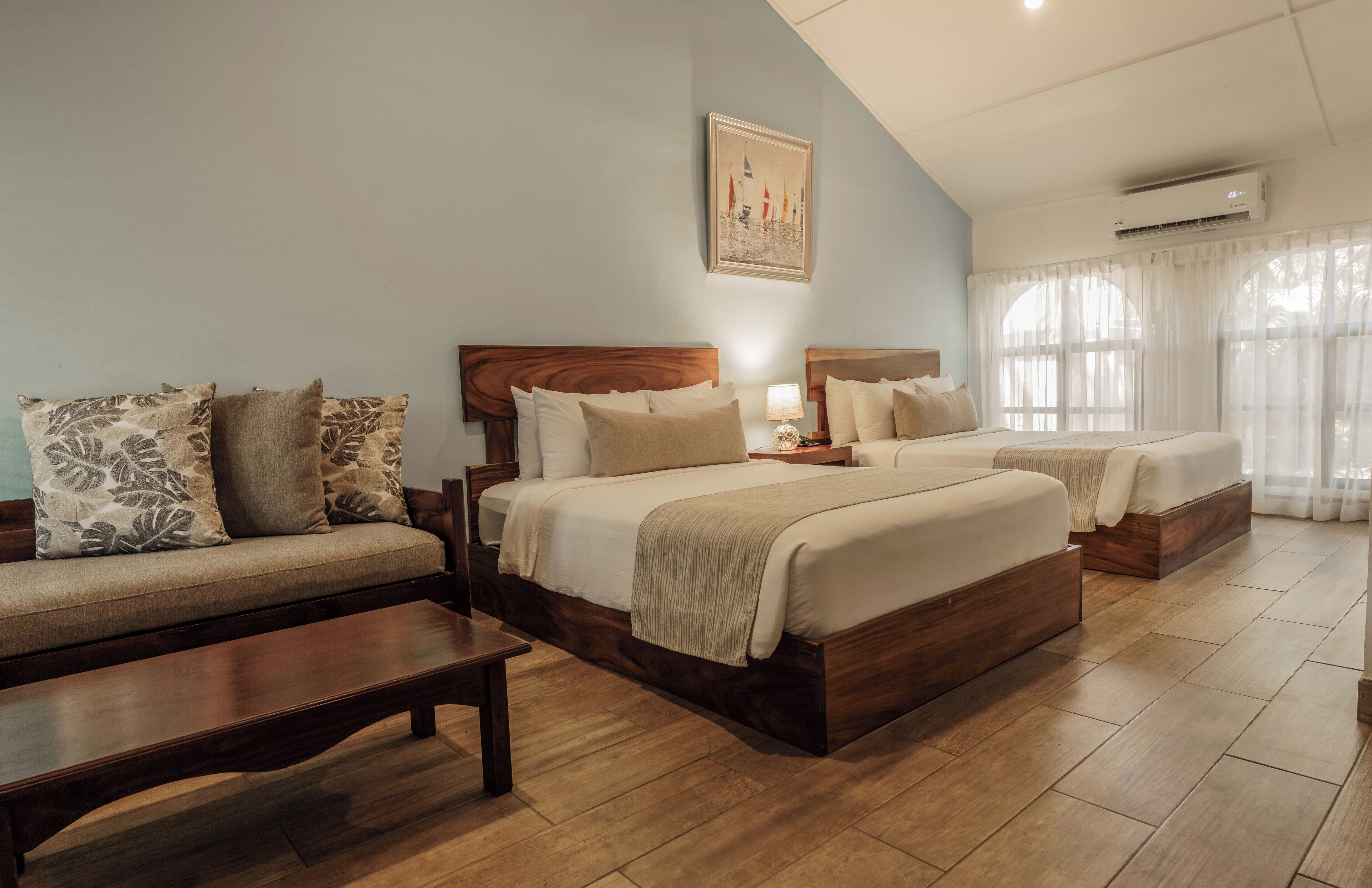 A bedroom with two beds, a sofa, a wooden bench, and a painting on the wall.