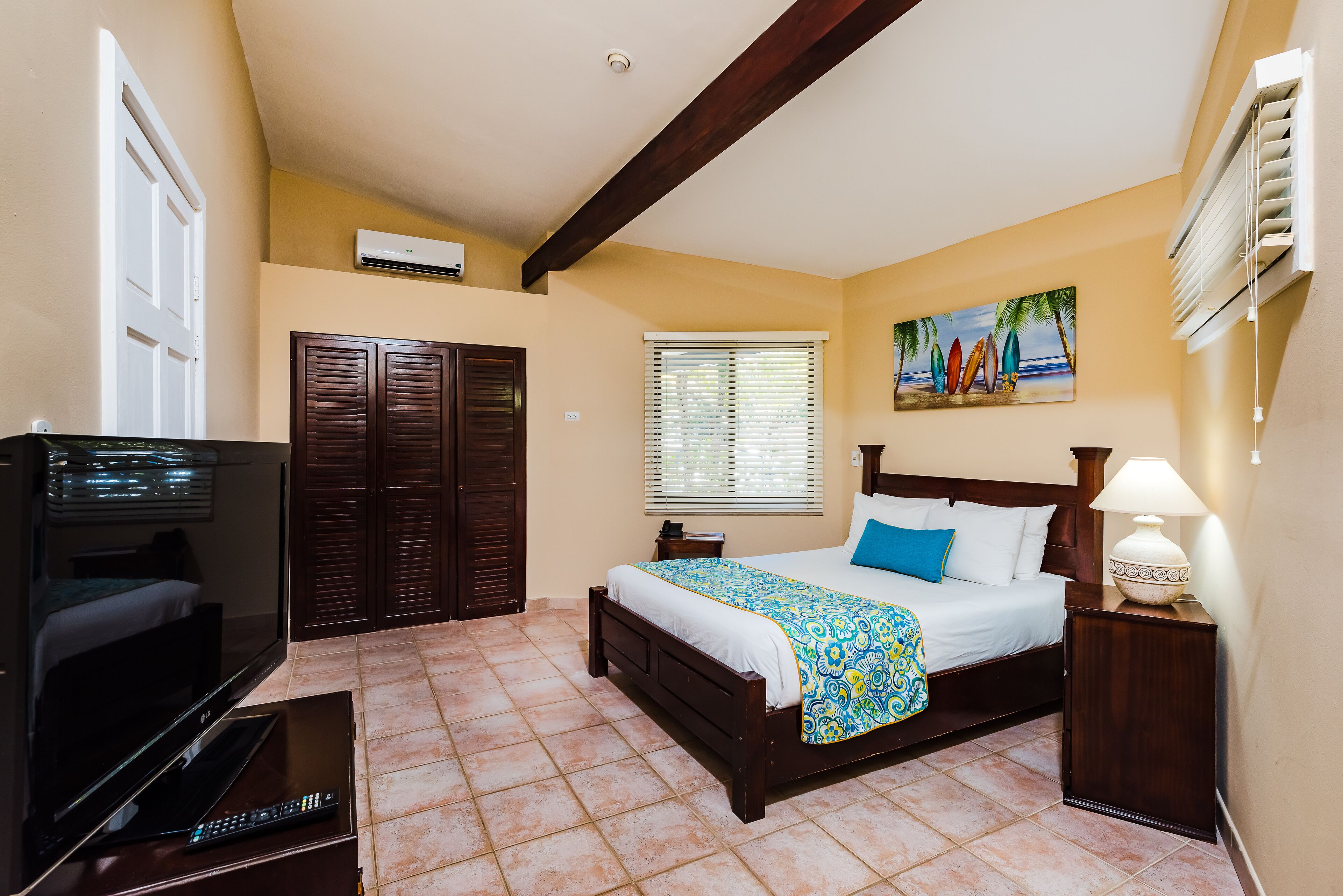 Un dormitorio con cama, televisión, escritorio y ventana con persianas.