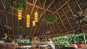 Een restaurant met rieten dak, hangplanten en houten meubilair.