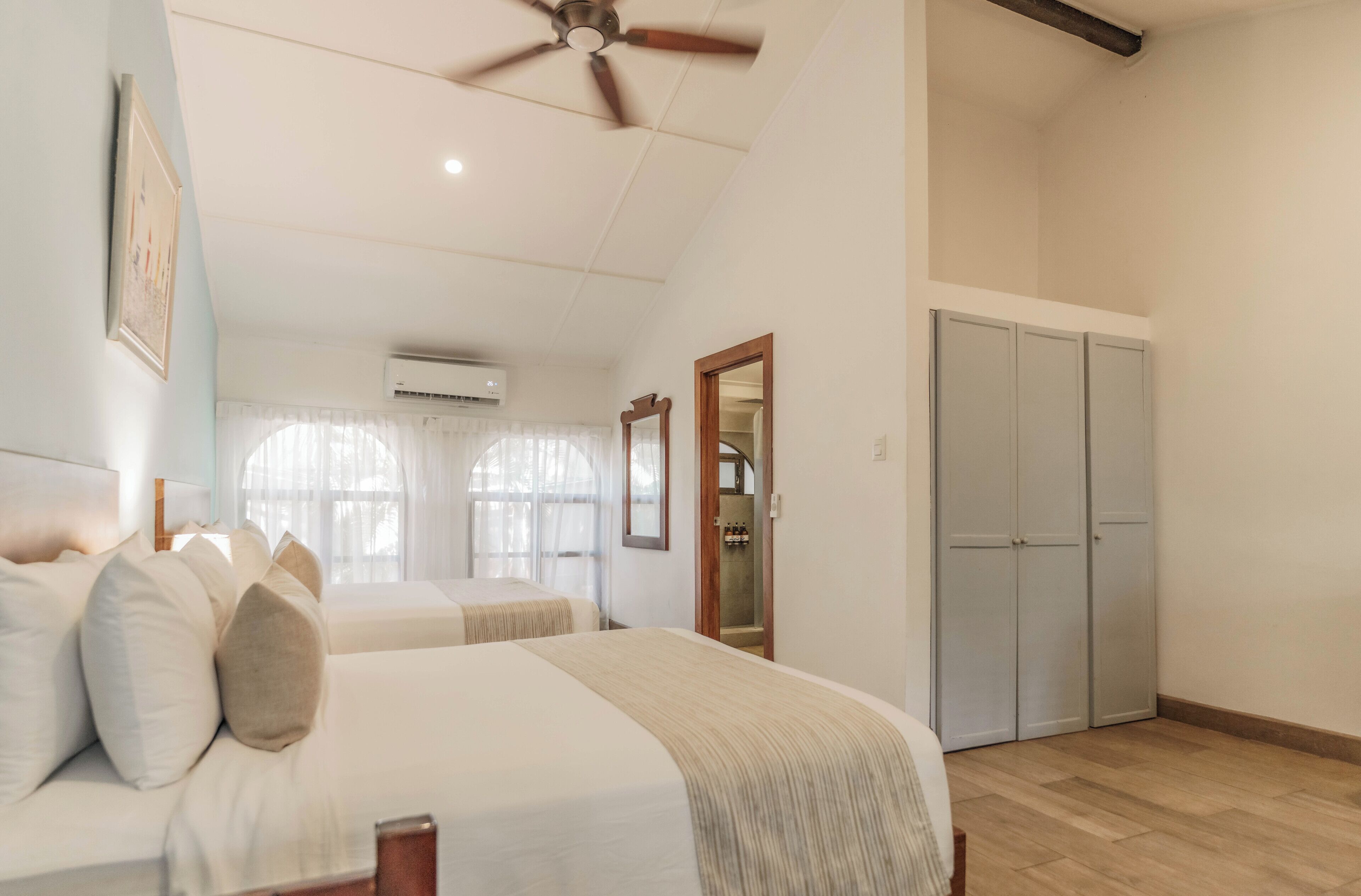 Une chambre avec deux lits, un ventilateur de plafond, un appareil de climatisation et une armoire.