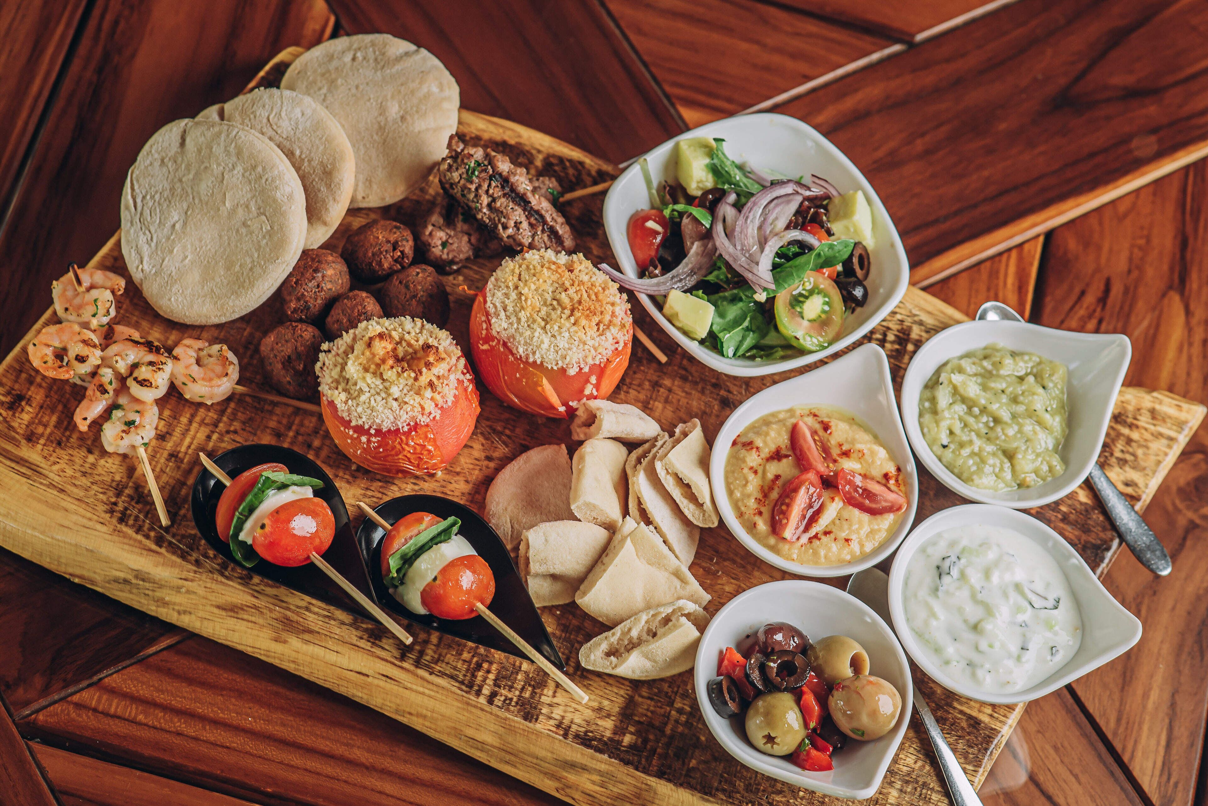 A wooden board with various foods including bread, meatballs, and vegetables.
