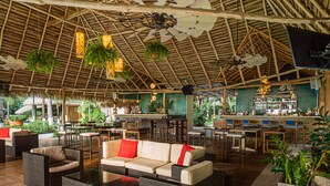 Ruime binnenruimte met een hoge plafond, bamboe balken, hangende planten en een bar met krukken en een aanrecht.