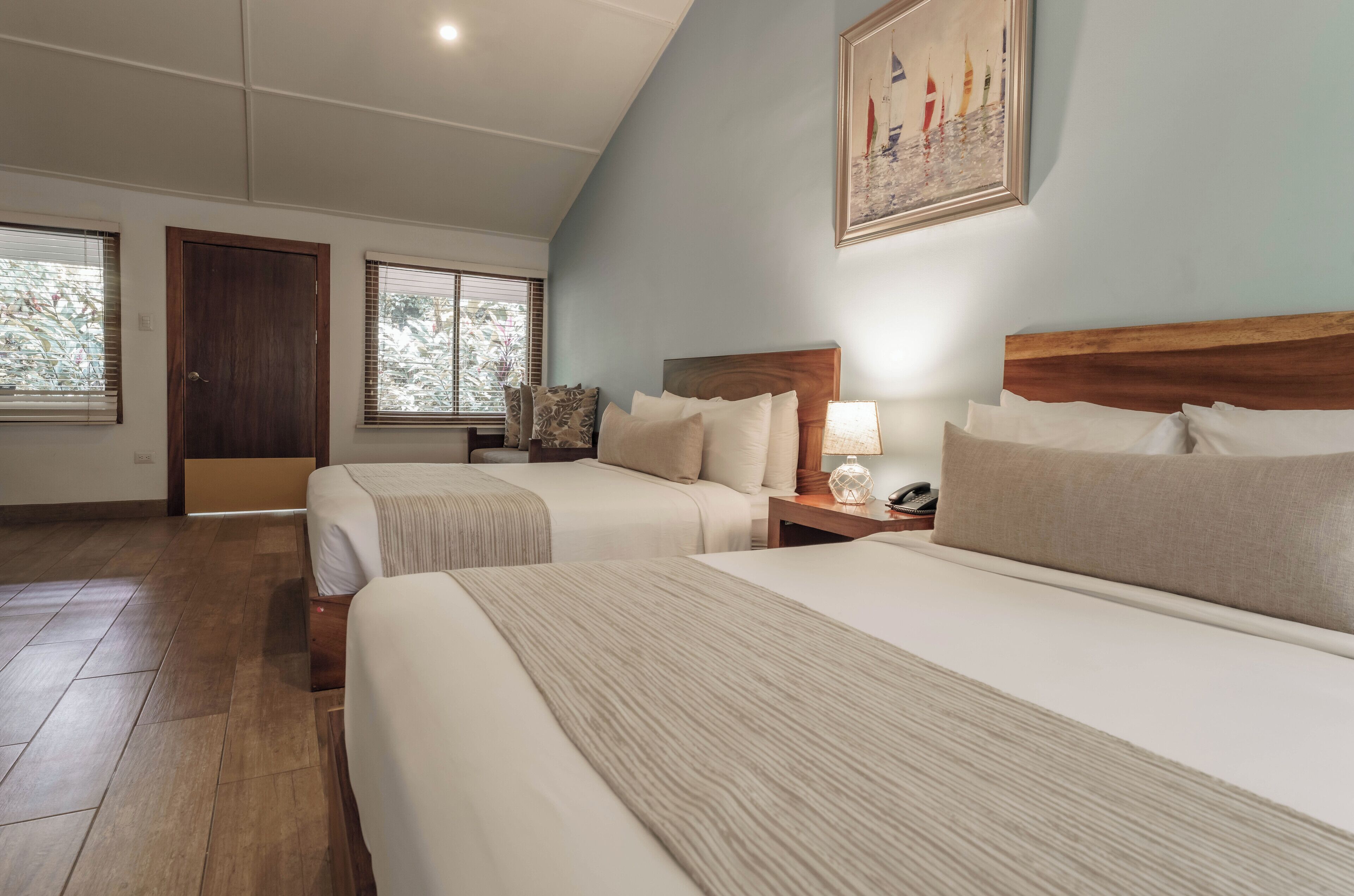 A hotel room with two beds, a wooden headboard, a nightstand with a lamp, and a painting on the wall.