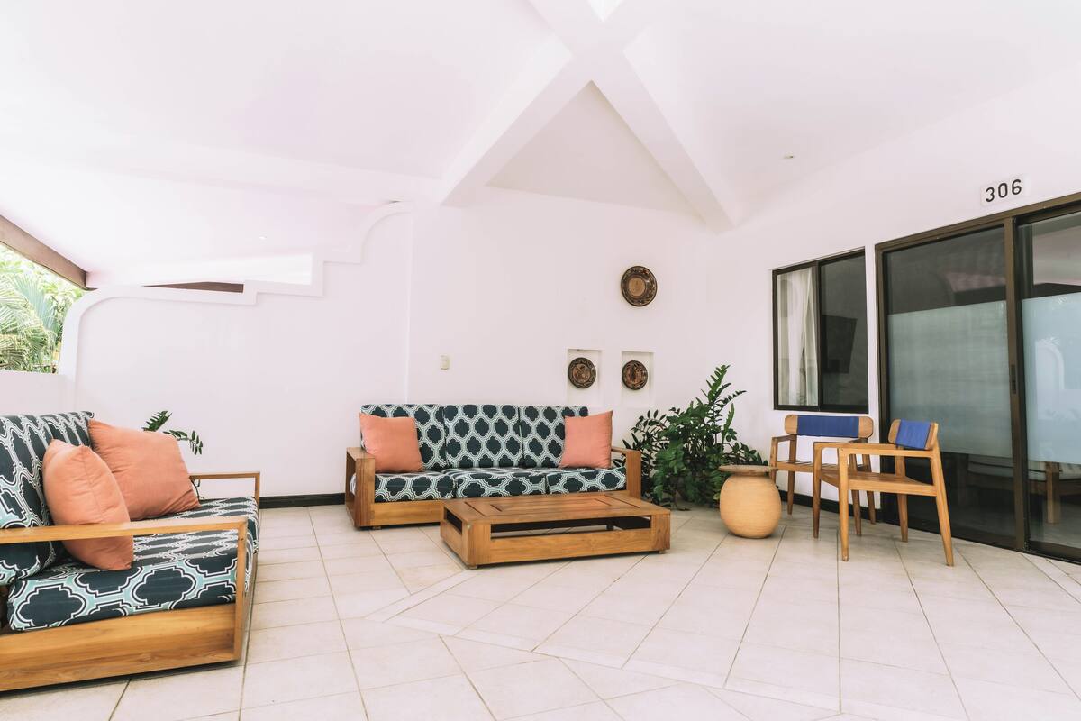 Un salon moderne avec un canapé, une table basse et des fauteuils, une grande fenêtre et une porte portant le numéro 306.