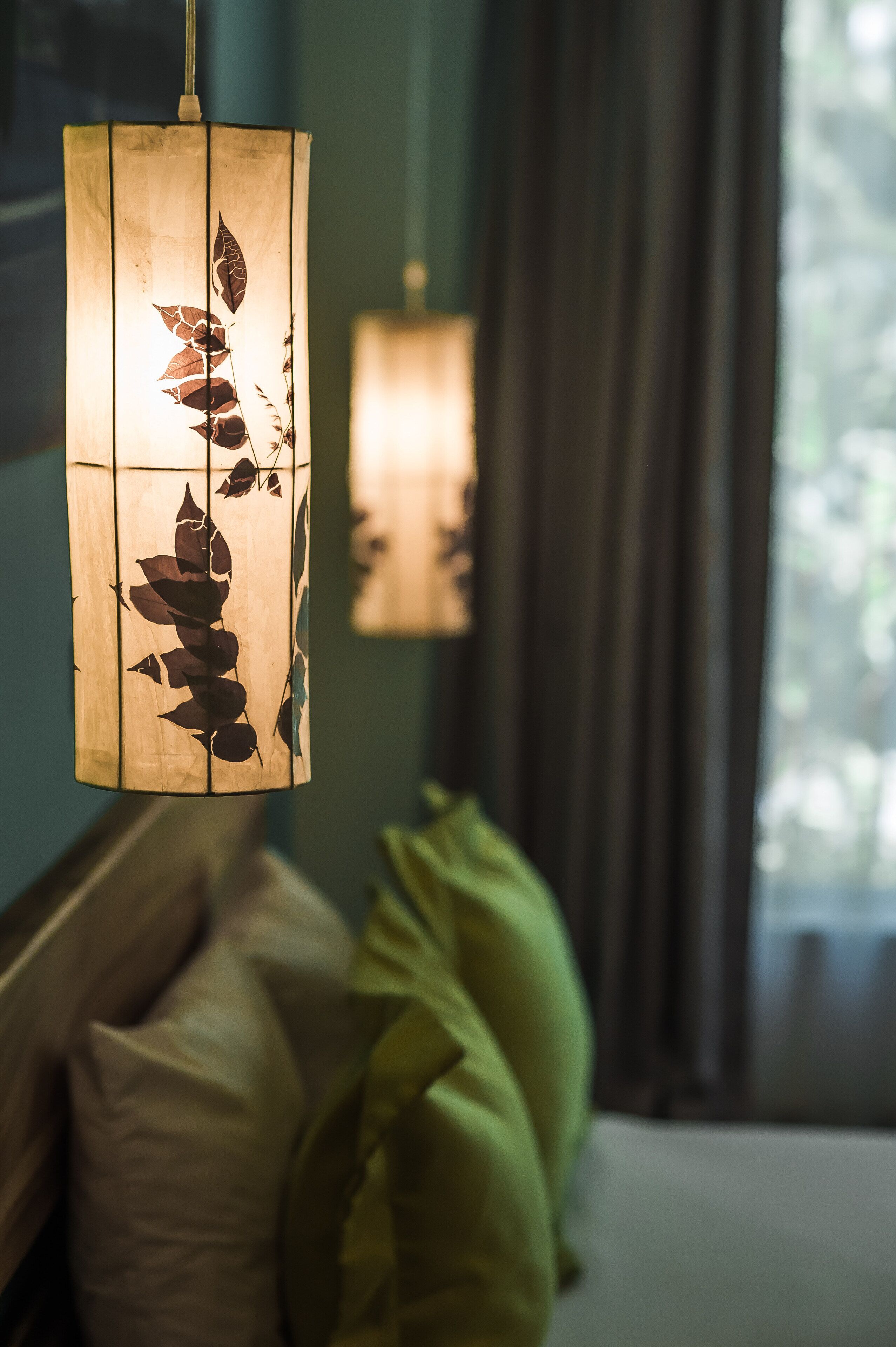 A hanging lamp with a leaf pattern, a bed with pillows, and a window with curtains.