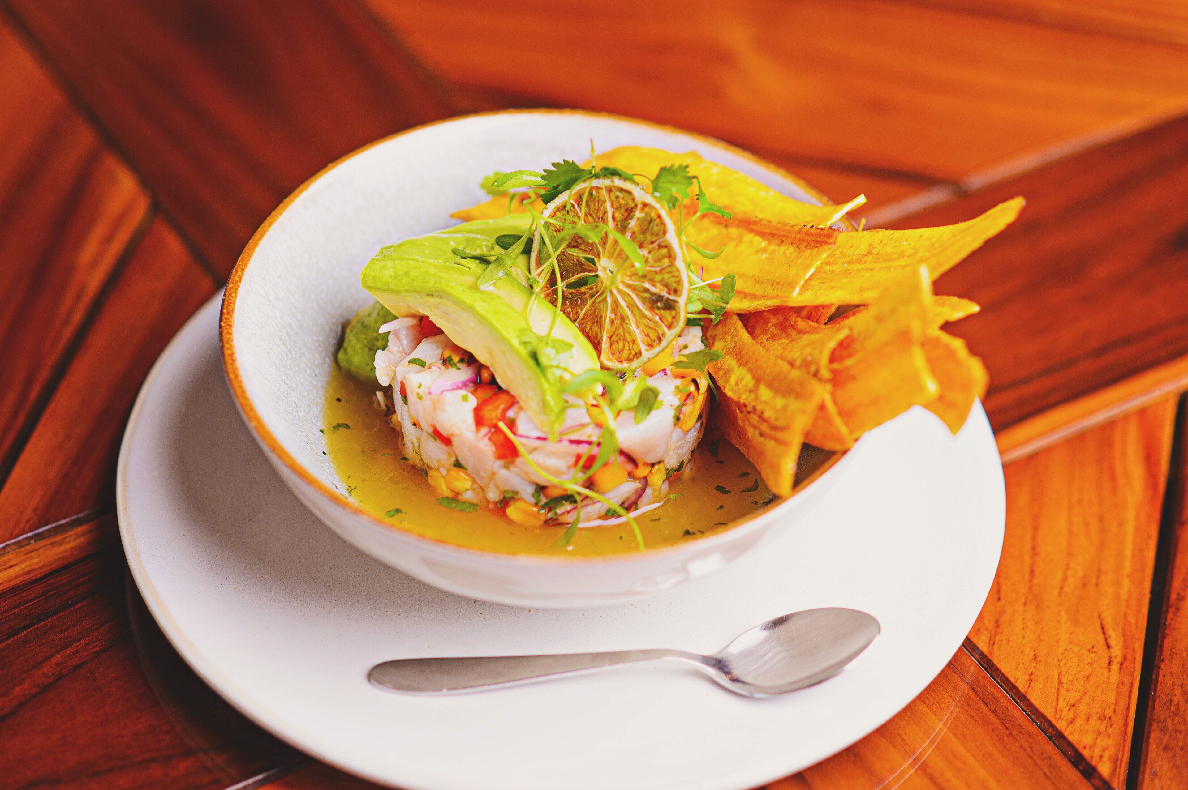 A bowl of seafood salad on a white plate with a spoon, set on a wooden table.
