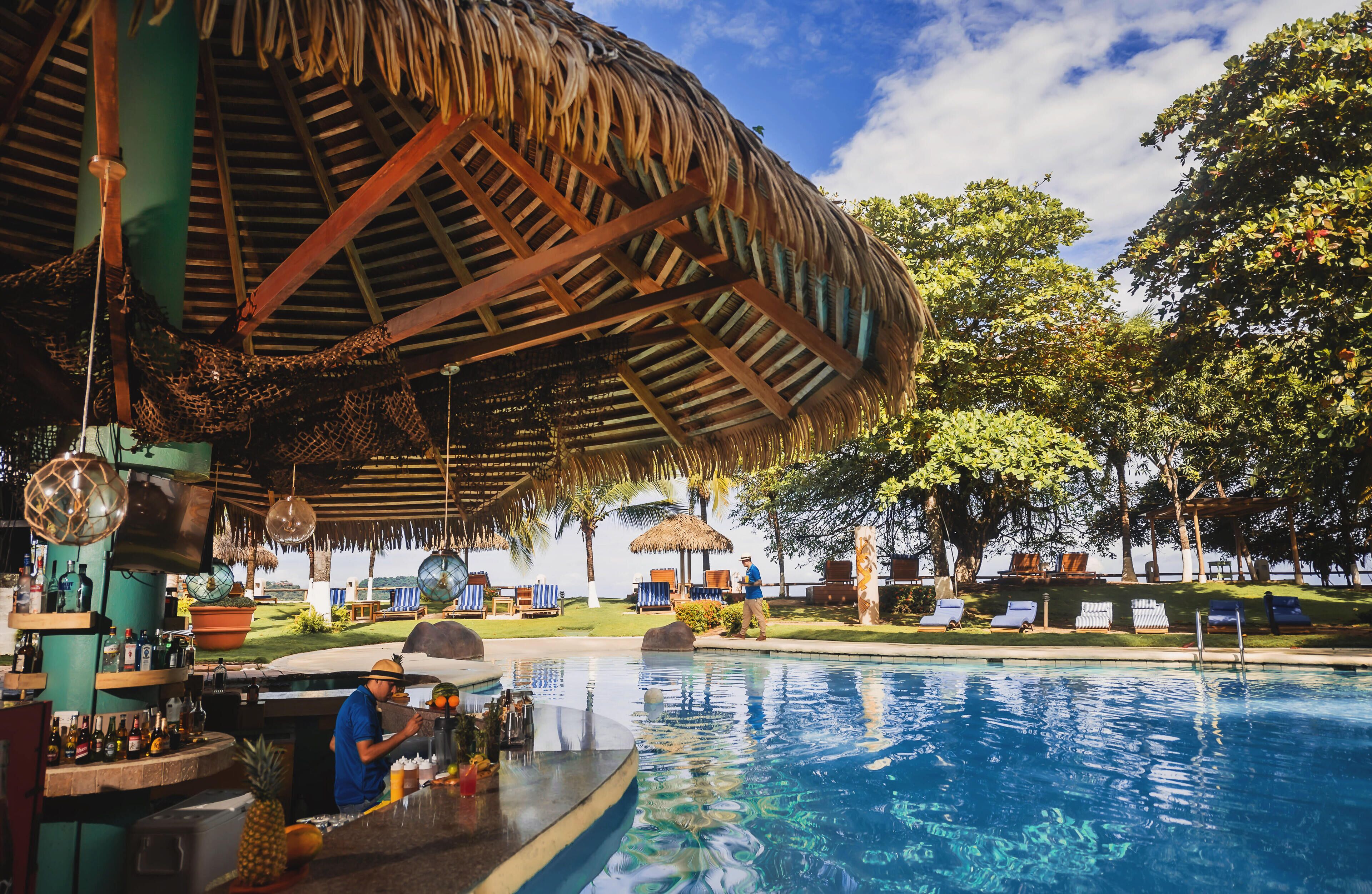 A poolside area with a bar, lounge chairs, and a thatched roof structure.