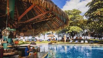 A poolside area with a bar, lounge chairs, and a thatched roof structure.