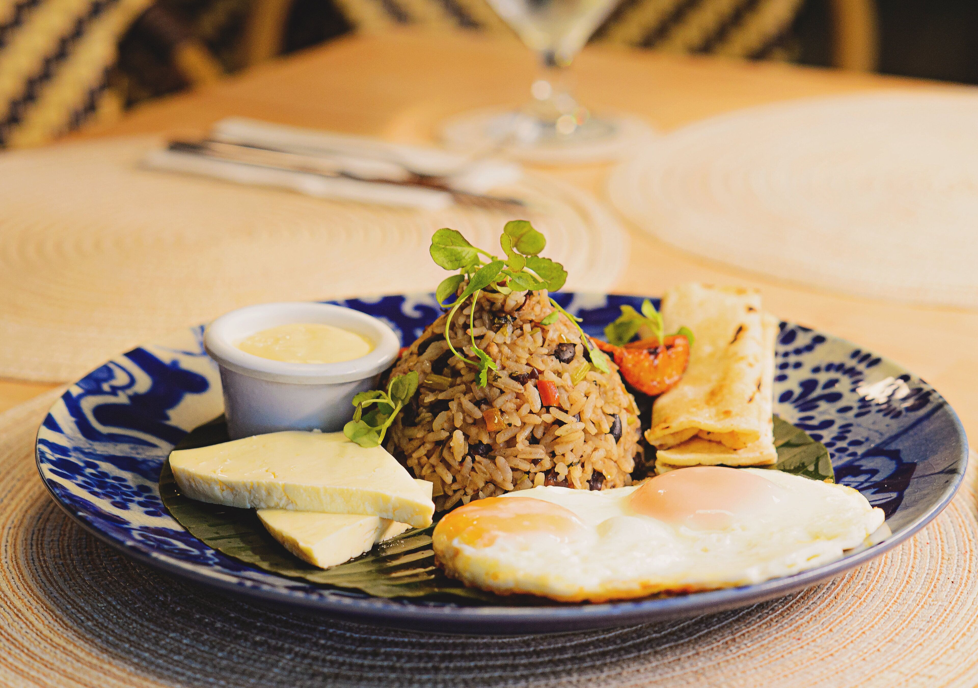 A plate of fried rice with vegetables, a fried egg, and a piece of flatbread on a blue and white patterned plate.