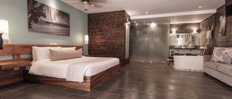 Une chambre moderne avec un grand lit, une tête de lit en bois, un ventilateur de plafond et une salle de bain dotée d’un grand lavabo et d’un grand miroir.