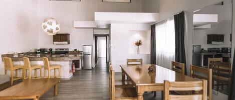 Un vaste espace de salle à manger avec une longue table et des chaises en bois, un coin cuisine doté de plans de travail en granit et un design moderne au décor minimaliste.