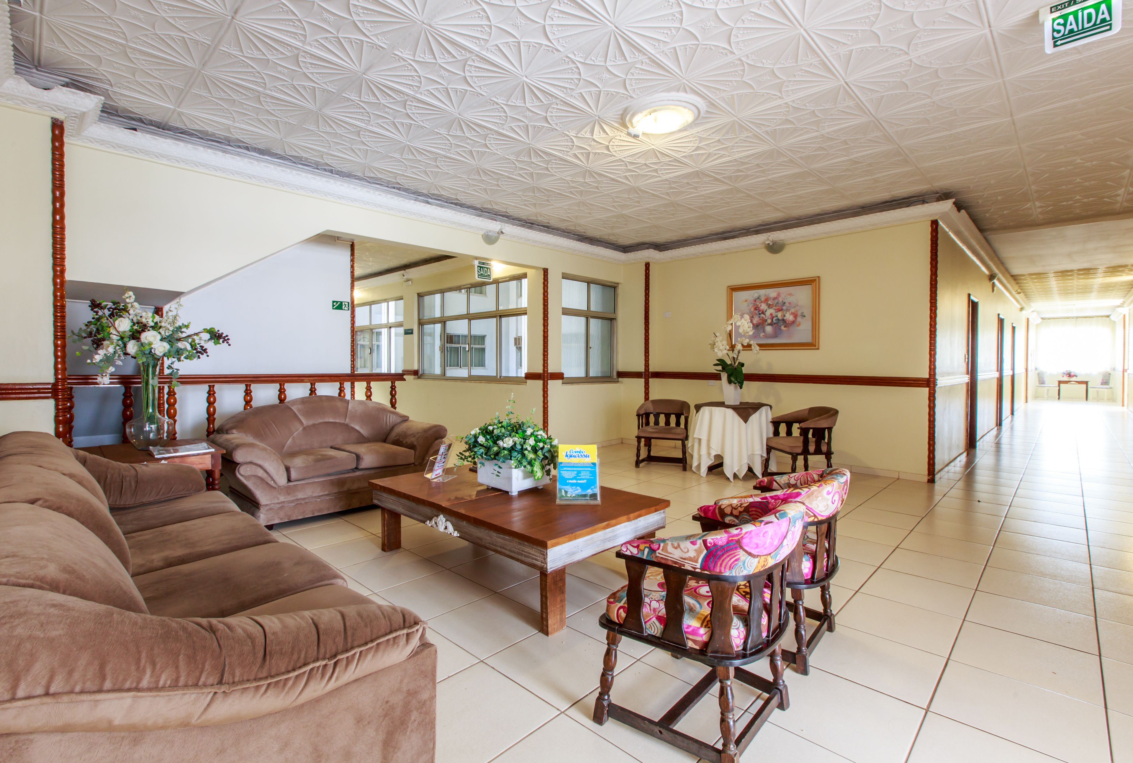 Eine geräumige Lobby mit hoher Decke, einem Empfangstresen, einer Couch, einem Couchtisch und einem gemusterten Sessel.