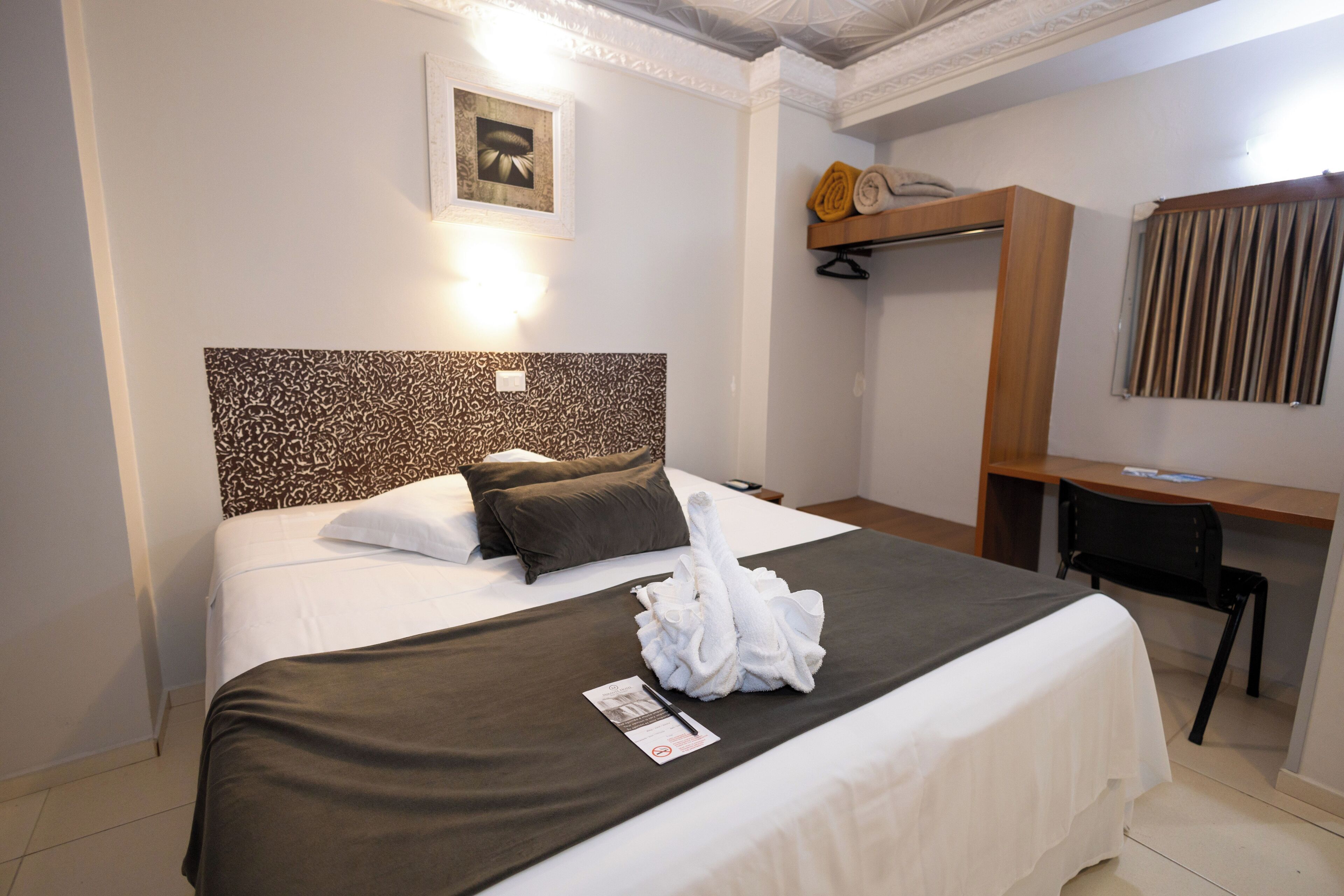 Ein Hotelzimmer mit einem aufgeräumten Bett, einem Schreibtisch und einem Stuhl.