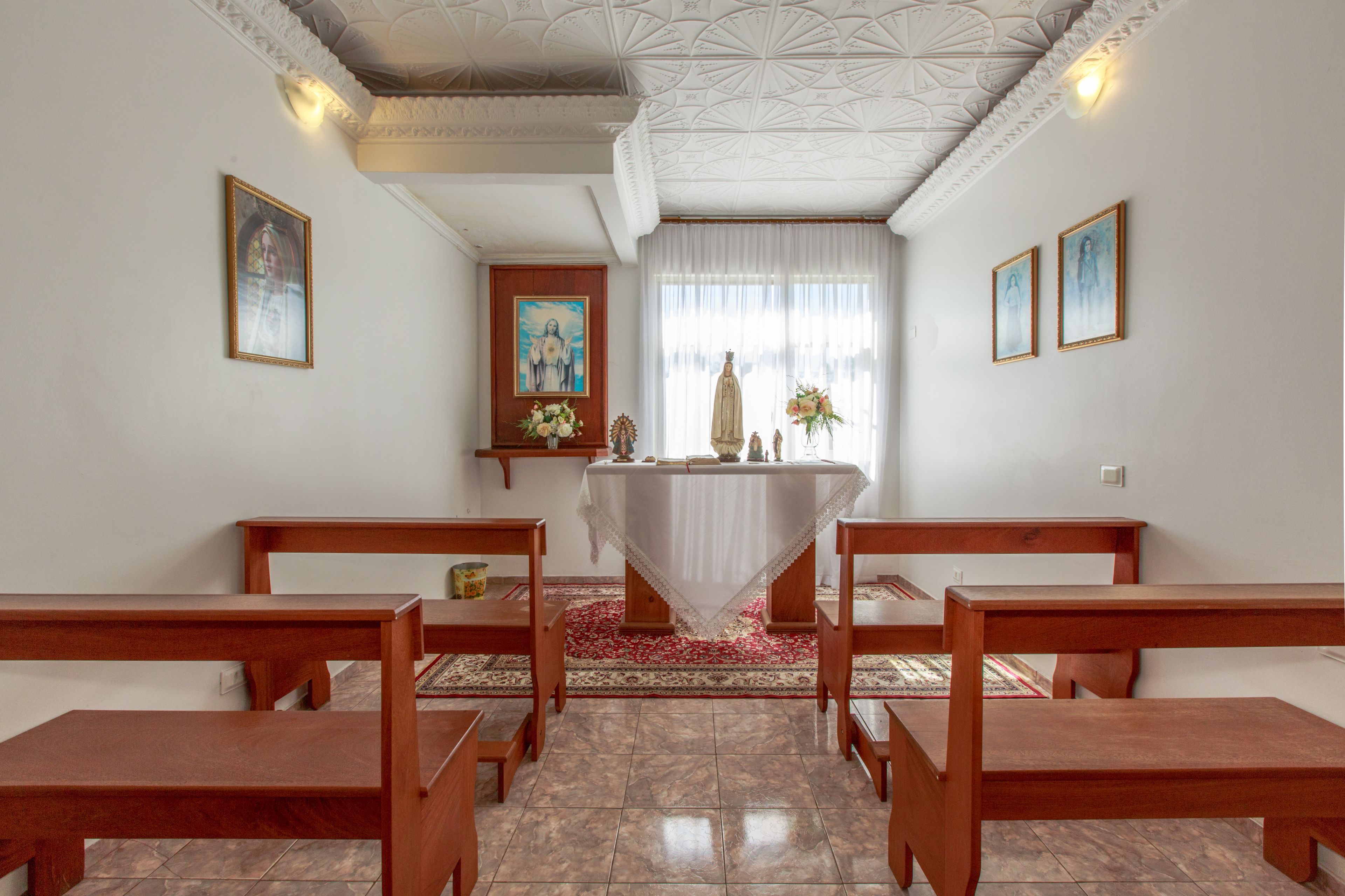 A chapel with wooden pews, a central altar, and religious paintings on the walls.