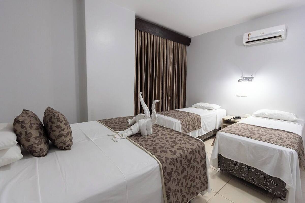 Een hotelkamer met twee bedden, een groot raam met gordijnen, een airconditioning en een nachtkastje met lamp.