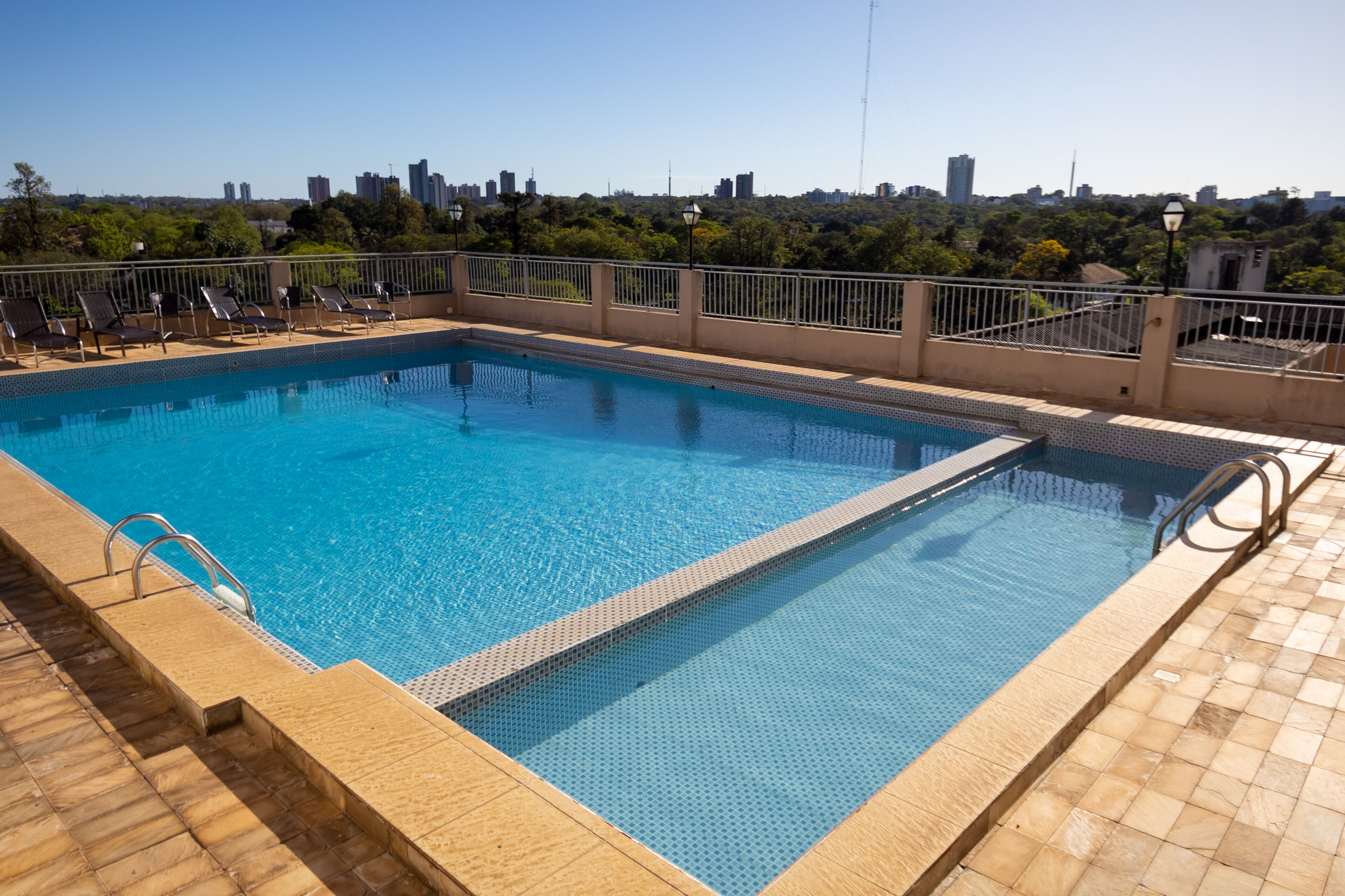 Una piscina rectangular con borde de azulejos y una escalera metálica en un lateral, rodeada de una solana con baldosas.