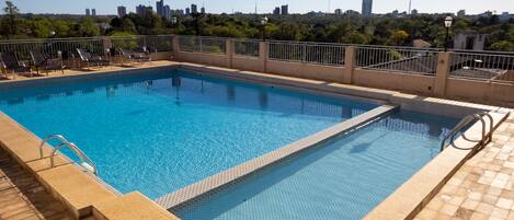 Una piscina rectangular con borde de azulejos y una escalera metálica en un lateral, rodeada de una solana con baldosas.