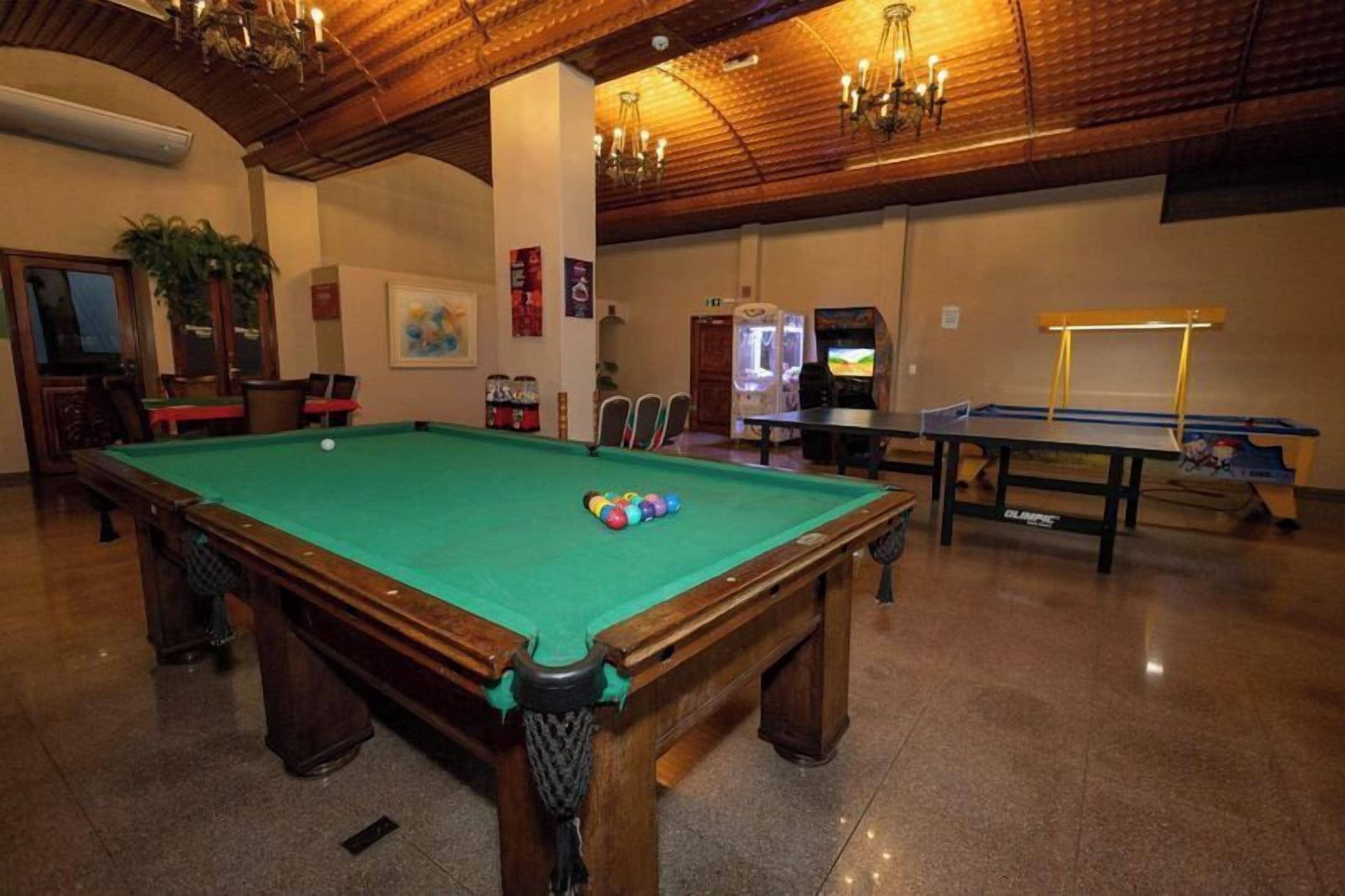 A pool table with balls, a billiards table, and a pool table in a room with wooden ceilings and chandeliers.
