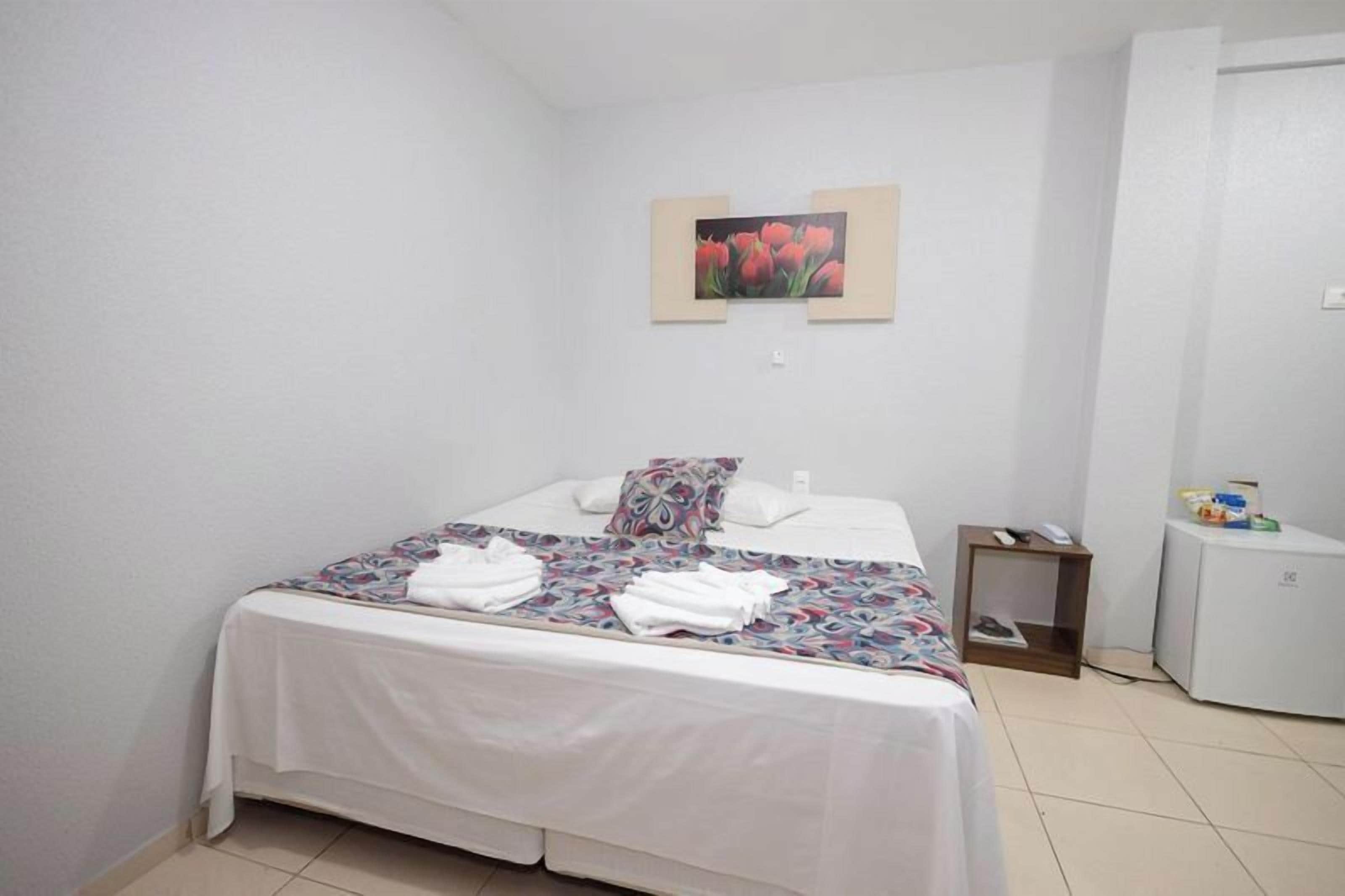 Una habitación de hotel con una cama, una mesita de noche, una pequeña mesa y un refrigerador.