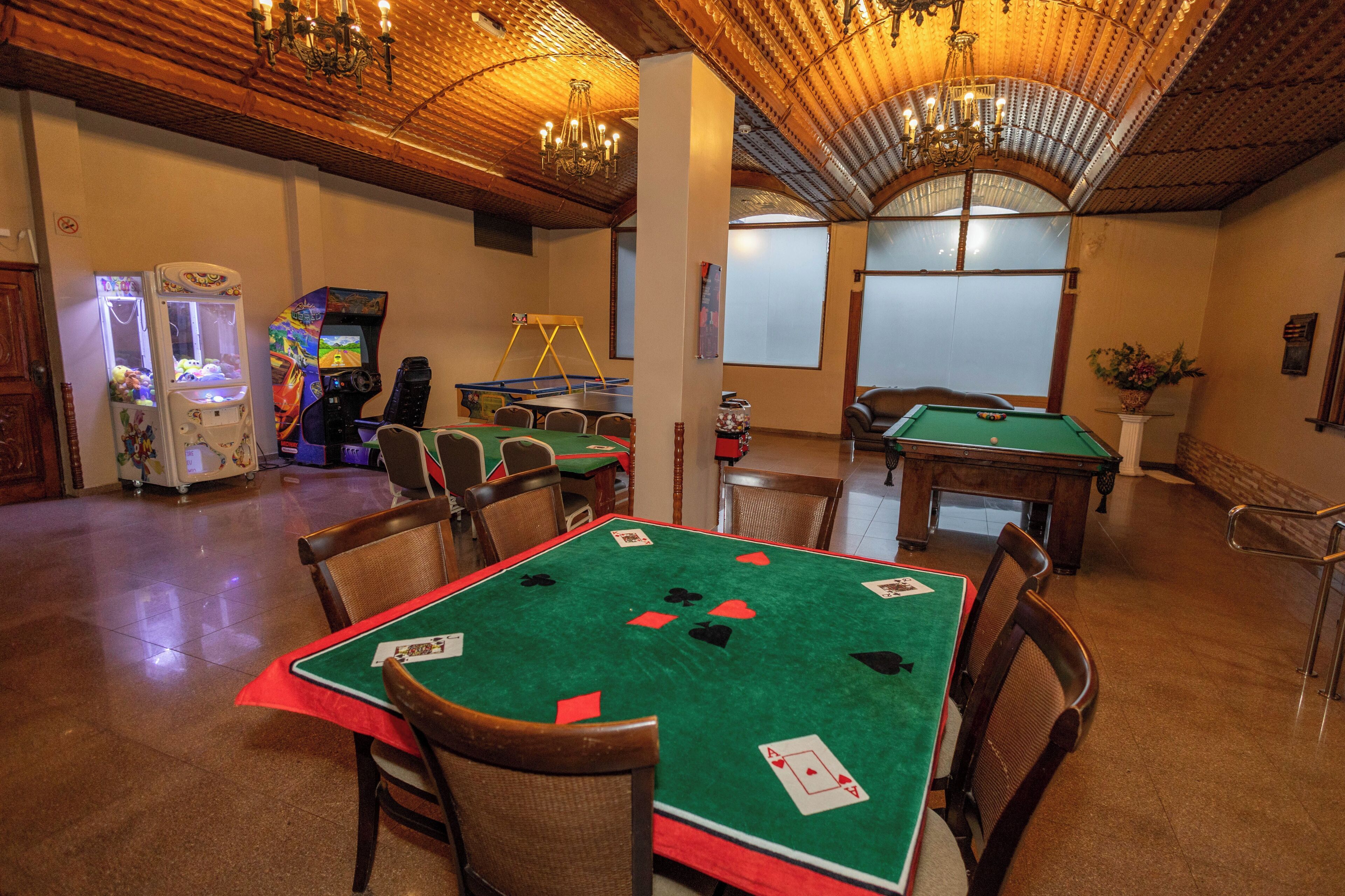 A room with a pool table, a green felt table for card games, and arcade machines.