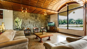 A spacious living room with a large television, comfortable sofas, a coffee table, and a stone wall with a mural.