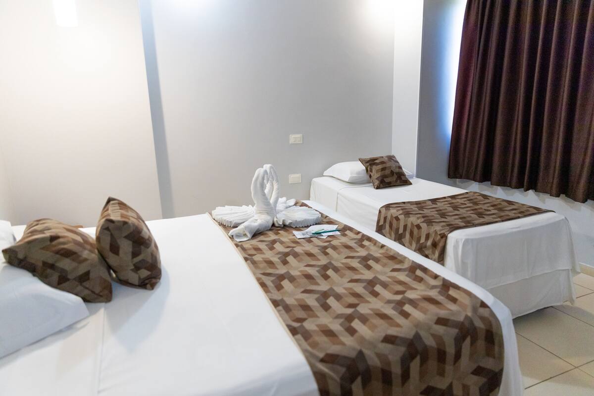 Een hotelkamer met twee bedden, elk voorzien van een beddekleed met dessin en kussens. Handdoeken liggen netjes opgemaakt op de bedden.