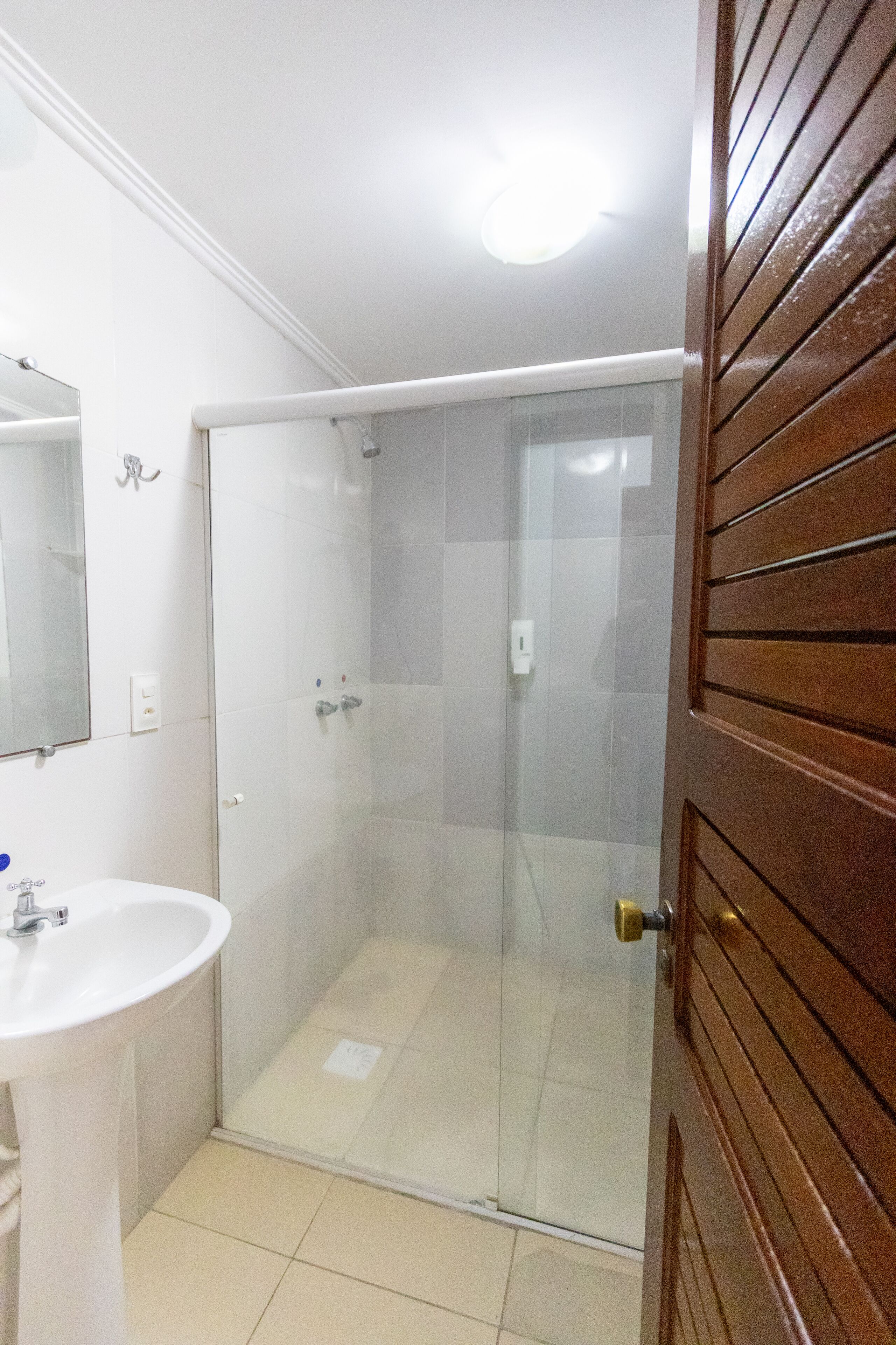 A bathroom with a white sink, a glass shower enclosure, and a wooden door.