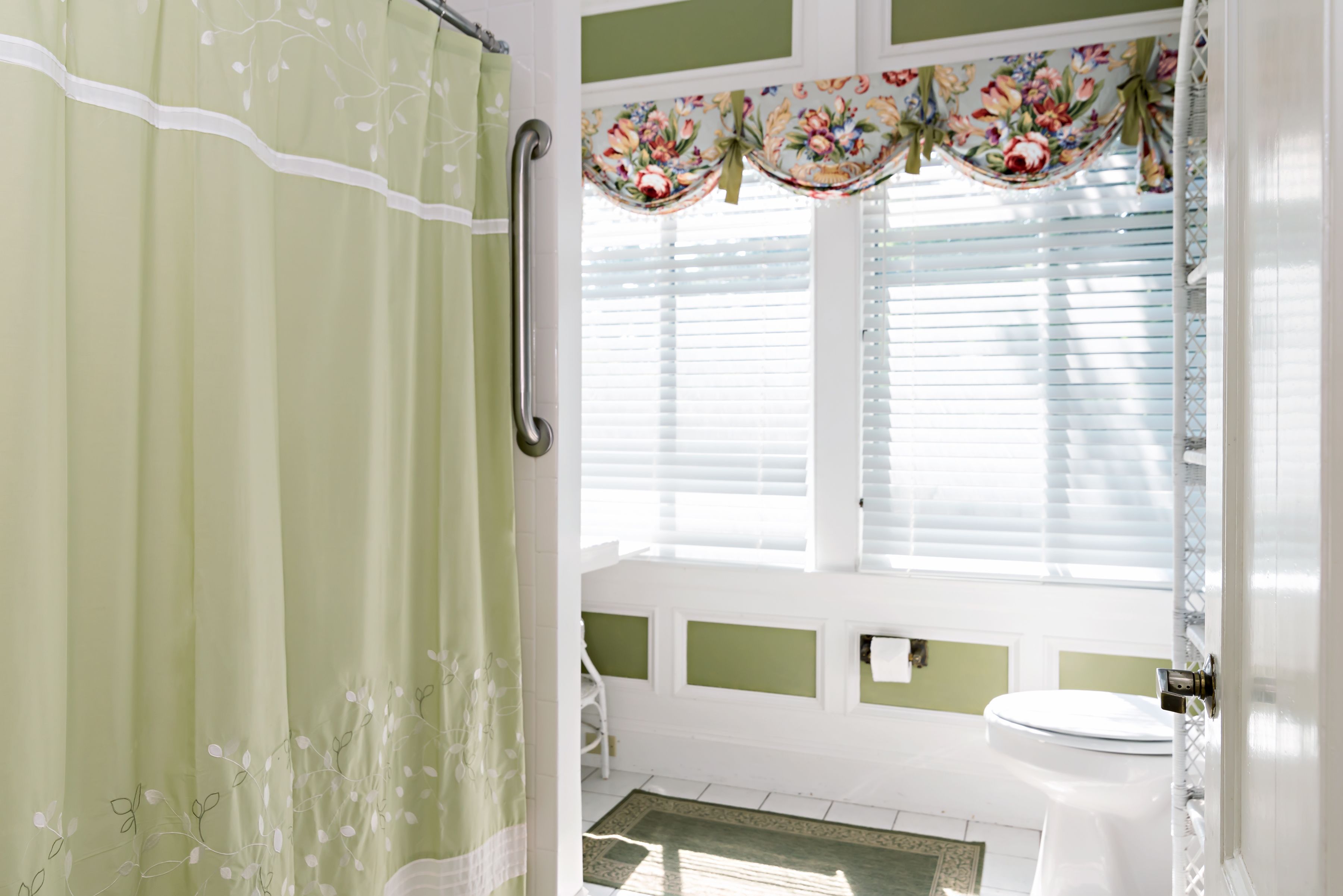 Un baño con cortina de ducha, inodoro y ventana con persianas.