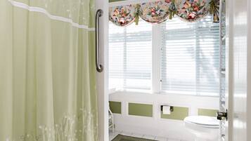 Un baño con cortina de ducha, inodoro y ventana con persianas.