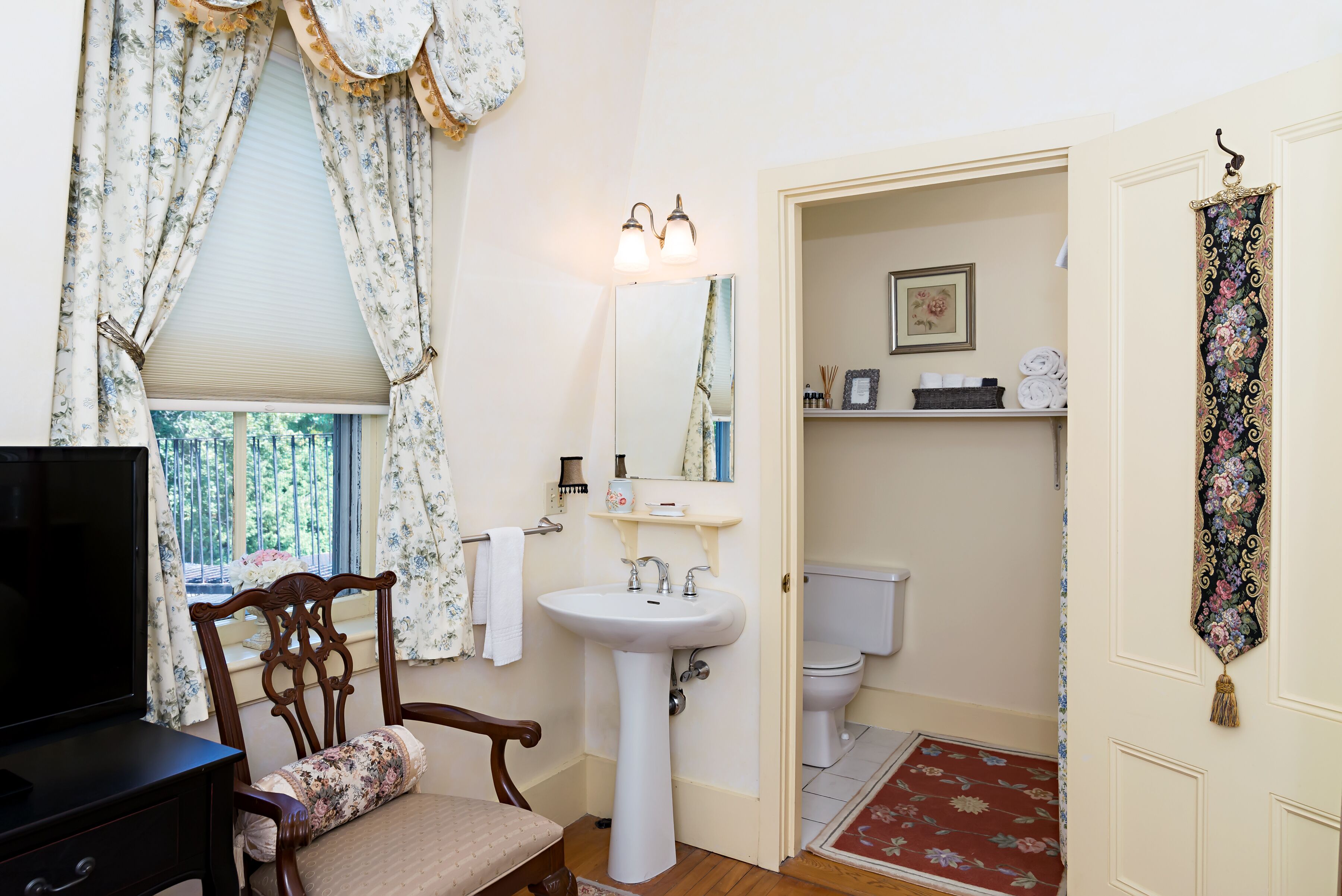 A bathroom with a wooden chair, a white sink, a mirror, and a toilet.