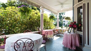 A covered porch with tables and chairs, surrounded by lush greenery and flowers.
