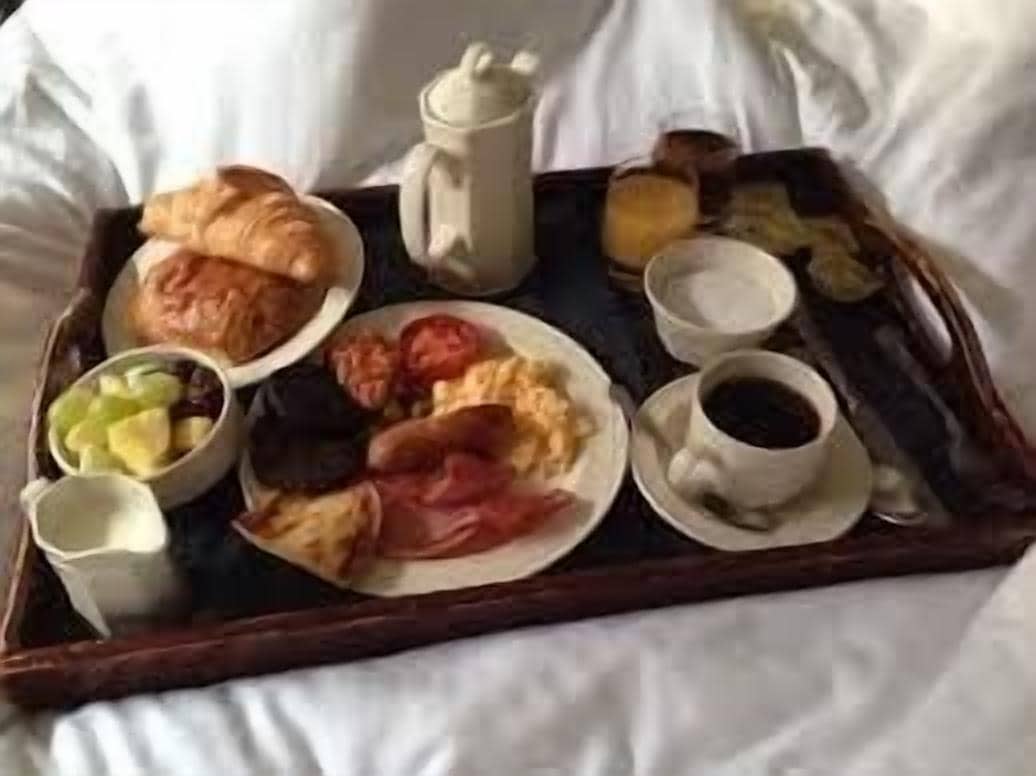 A tray with croissants, ham, eggs, and a cup of coffee on a bed.
