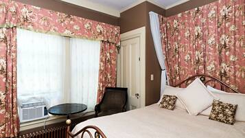 A bedroom with a bed, a chair, a table, and a radiator.