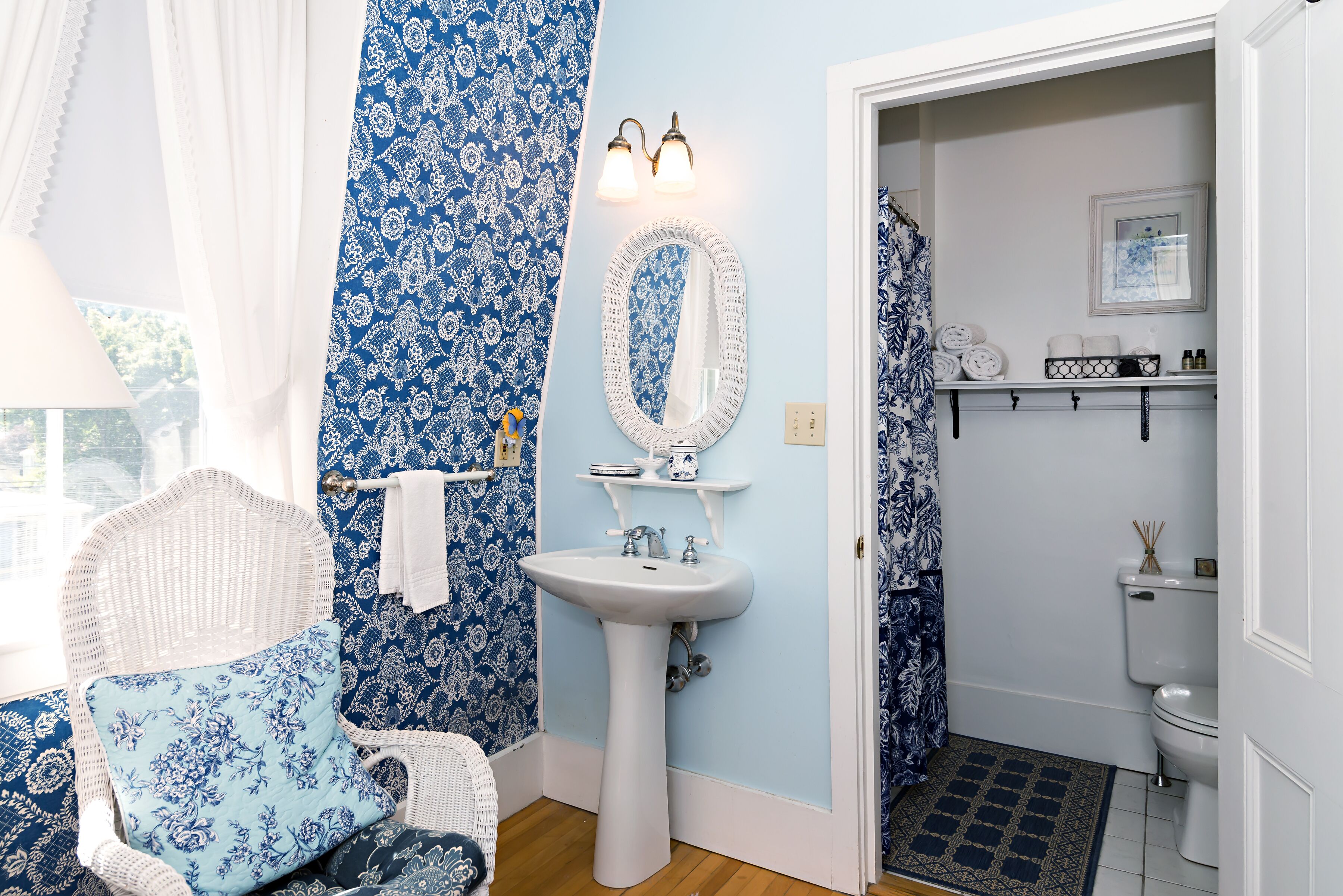 A bathroom with a white sink, blue patterned walls, a white chair, and a shower curtain.