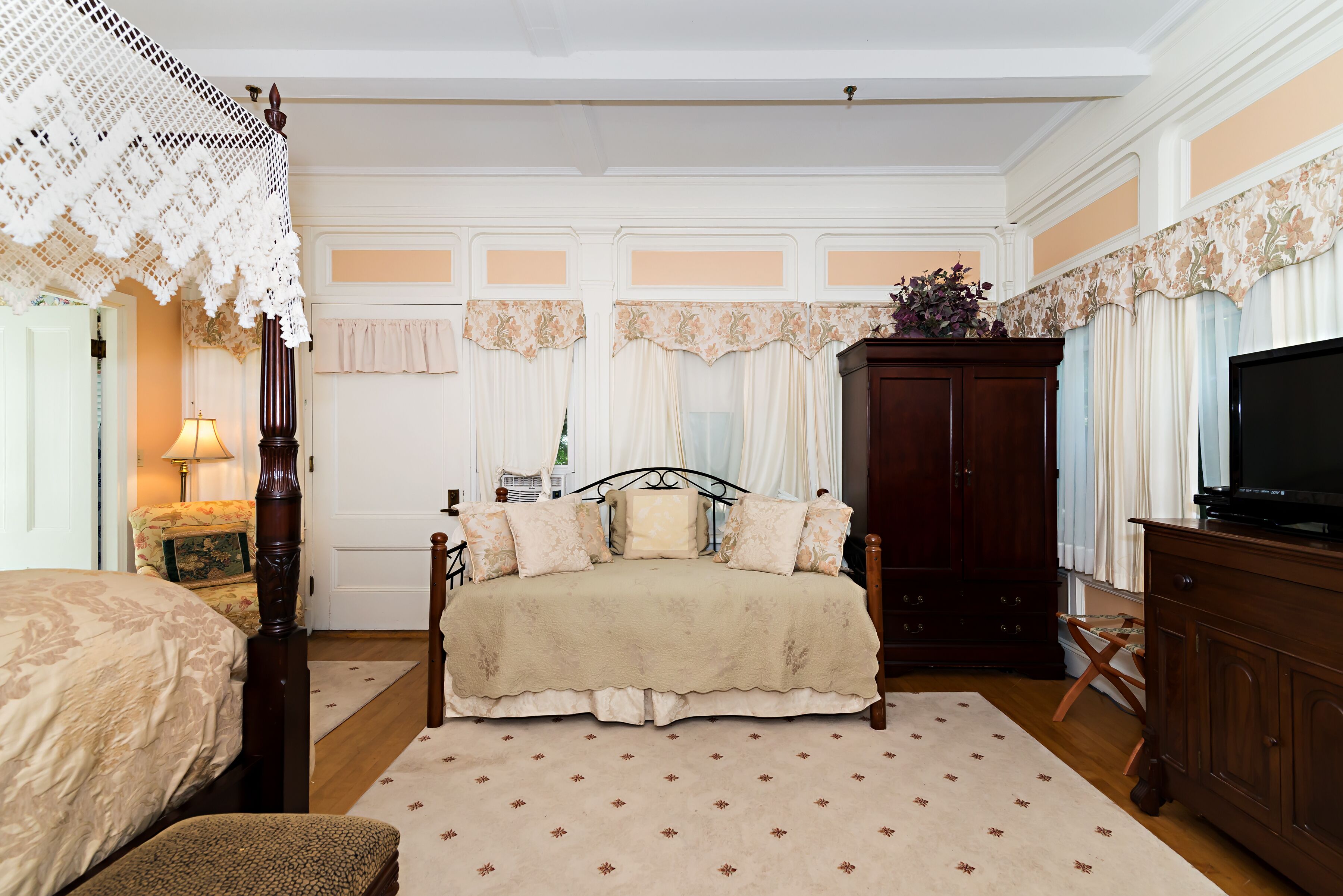 A bedroom with a large bed, a wooden wardrobe, a television, and a decorative lamp.