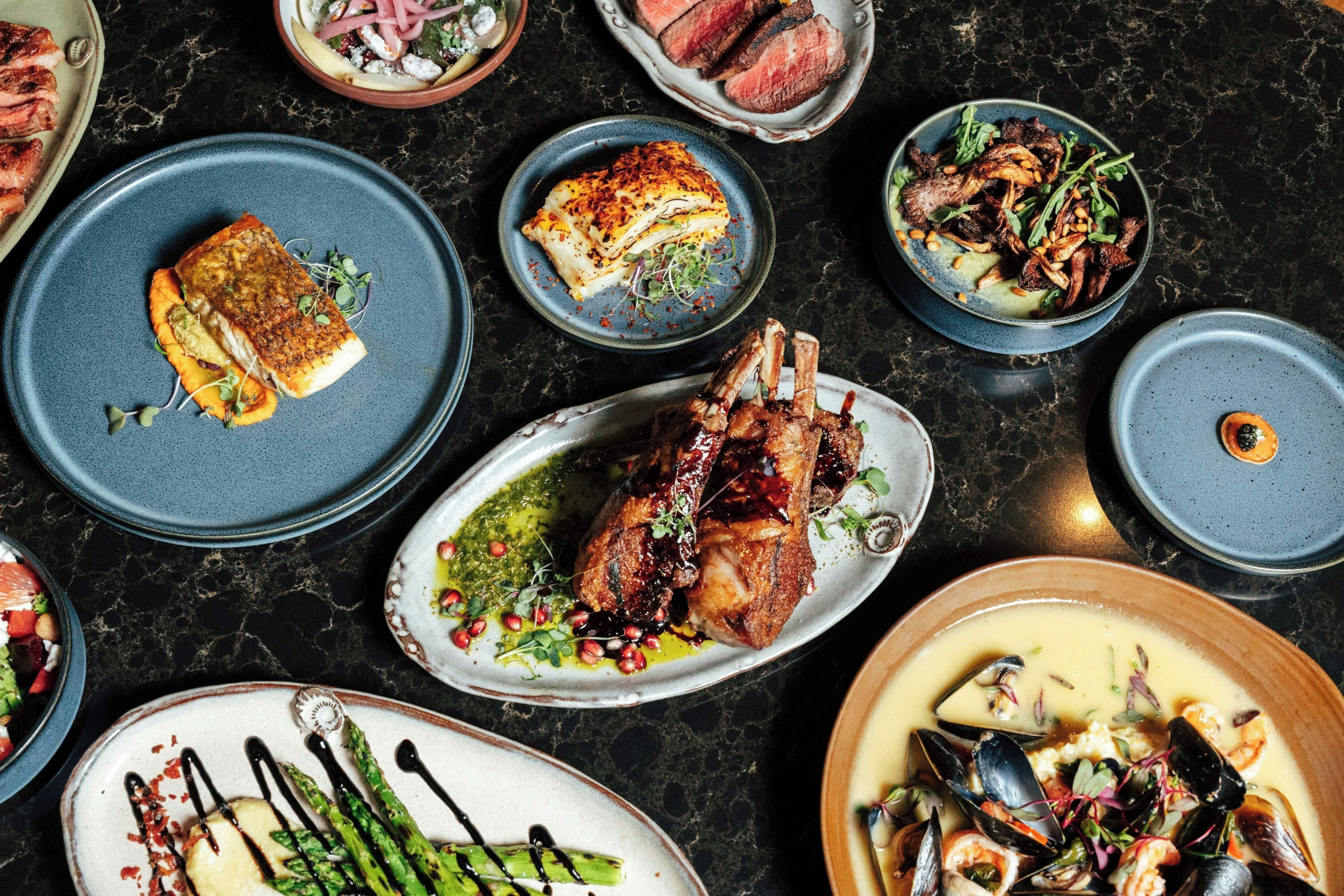 A variety of dishes on a dark marble table, including seafood, meat, and vegetables.