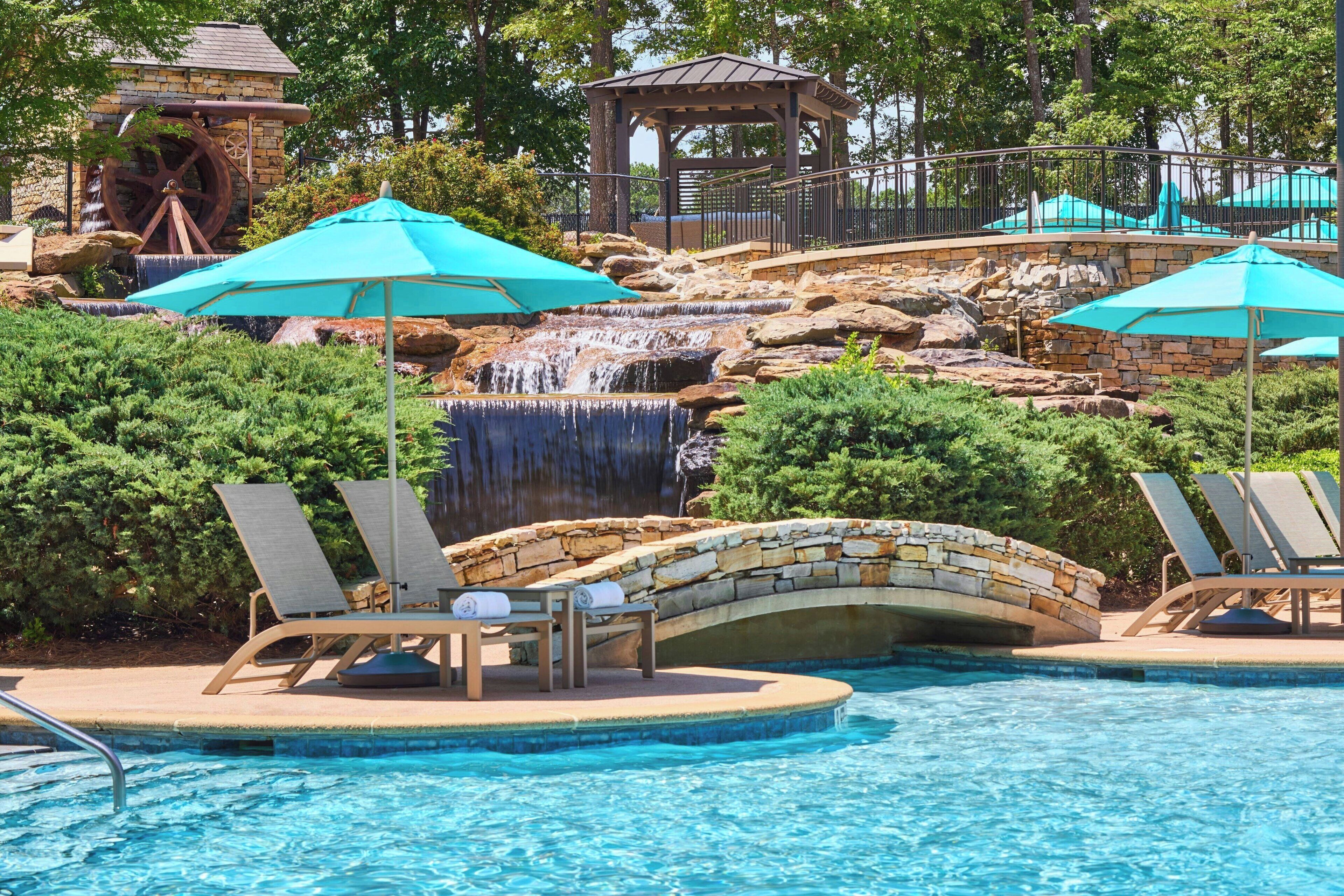 A pool area with a waterfall, lounge chairs, and umbrellas.