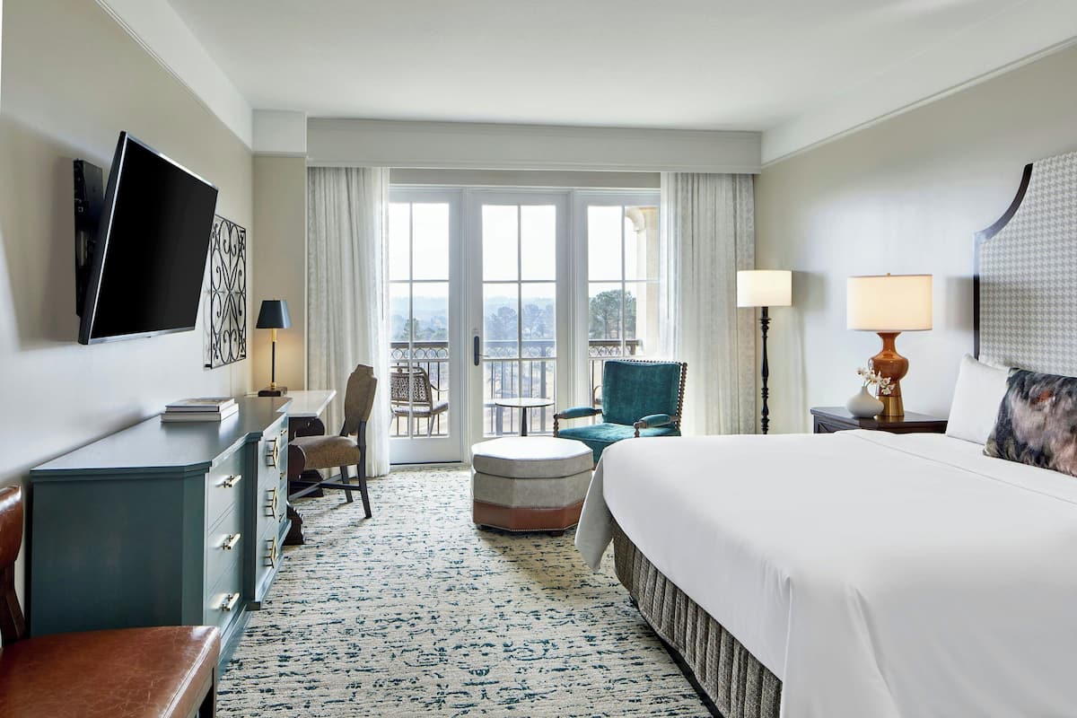 A hotel room with a bed, a desk, a chair, a small table, and a TV mounted on the wall.