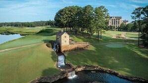 A golf course with a stone house, a pond, and a large building in the background. - Renaissance Birmingham Ross Bridge Golf Resort & Spa (Birmingham)