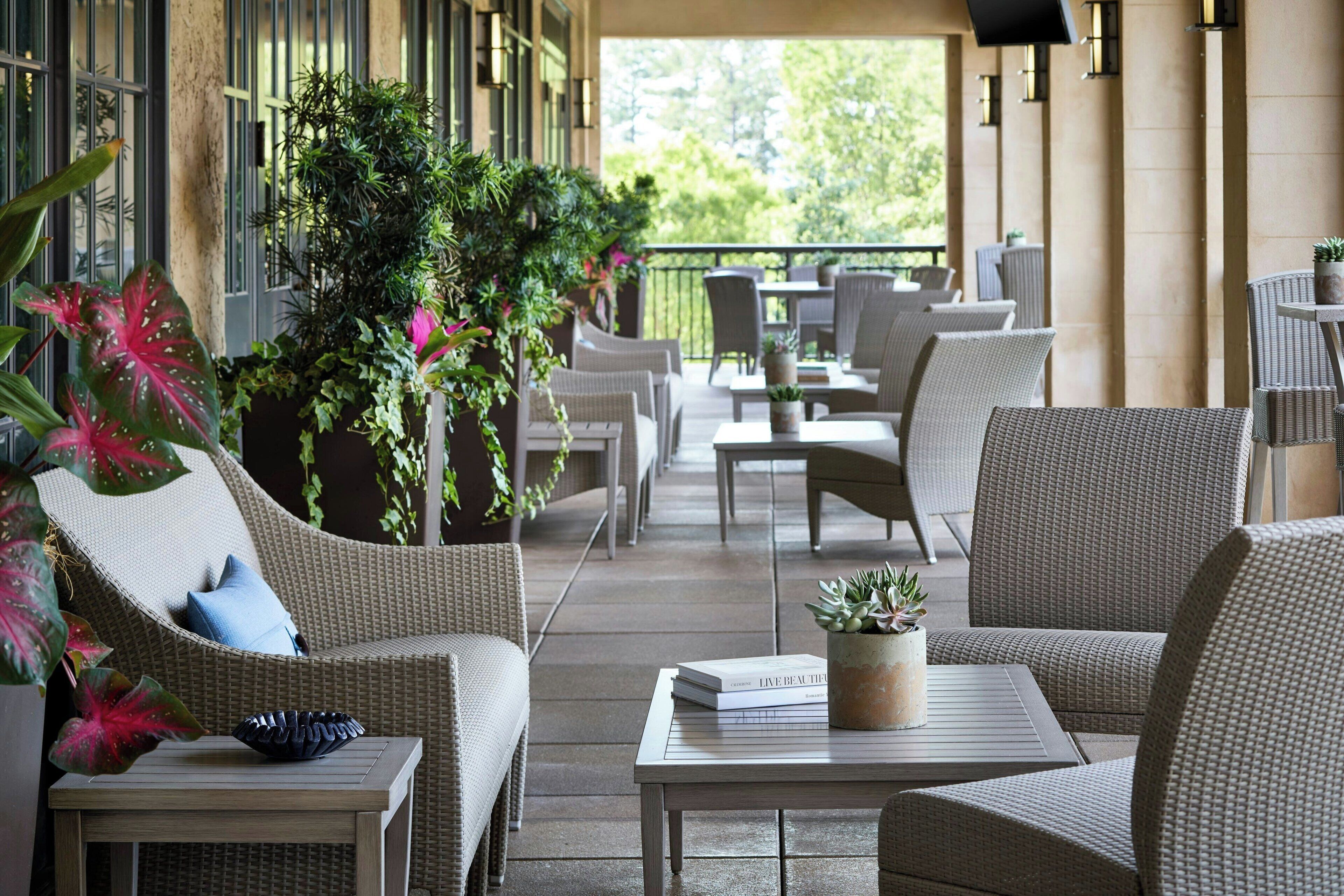 A covered outdoor seating area with wicker furniture, potted plants, and a table with a book.