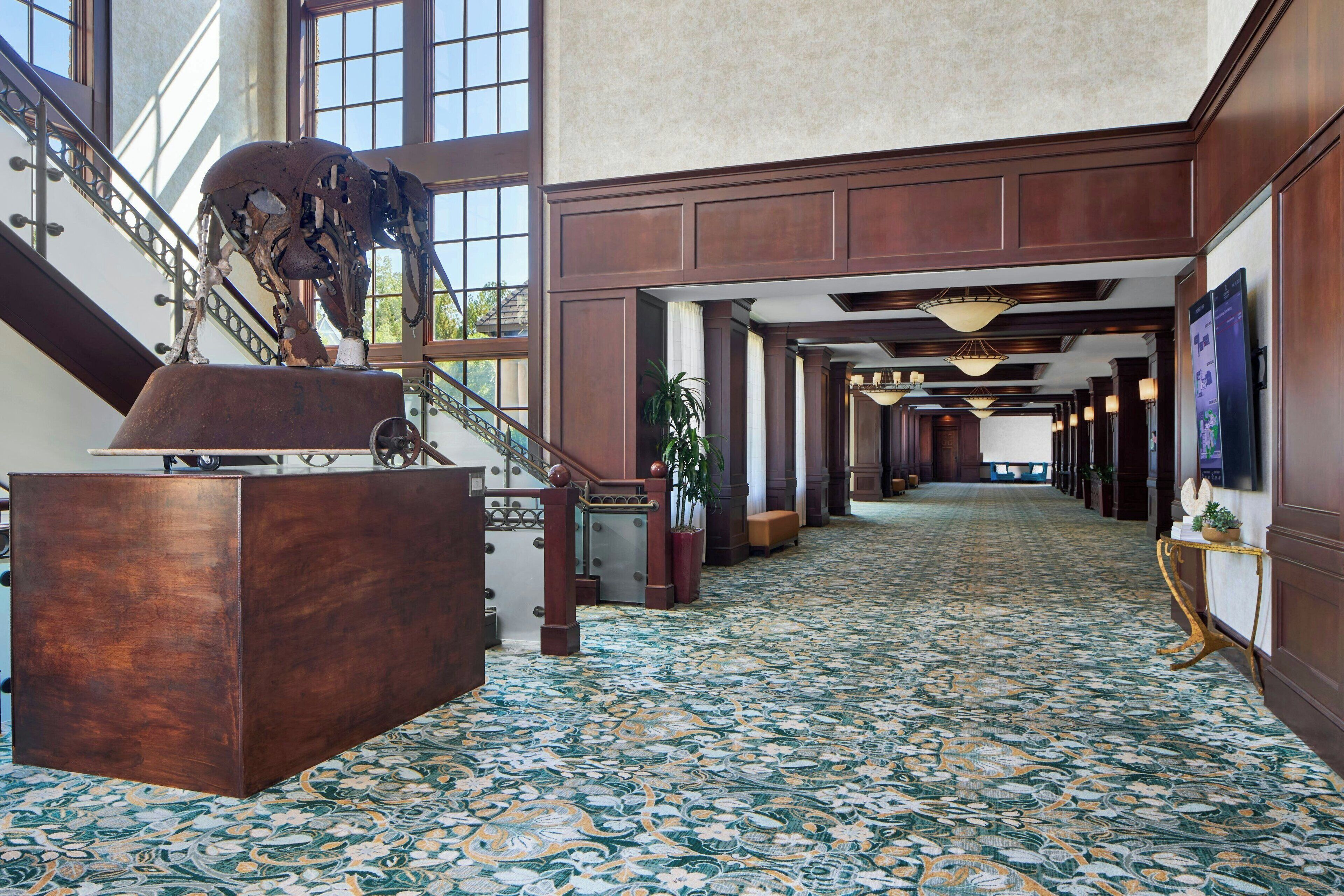 A spacious hallway with a patterned floor, a staircase with a metal railing, and a large wooden sculpture.