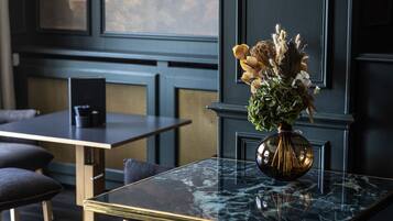 A modern room with a dark wood floor, a glass-top table with a gold frame, a dark blue wall, and a vase with dried flowers.