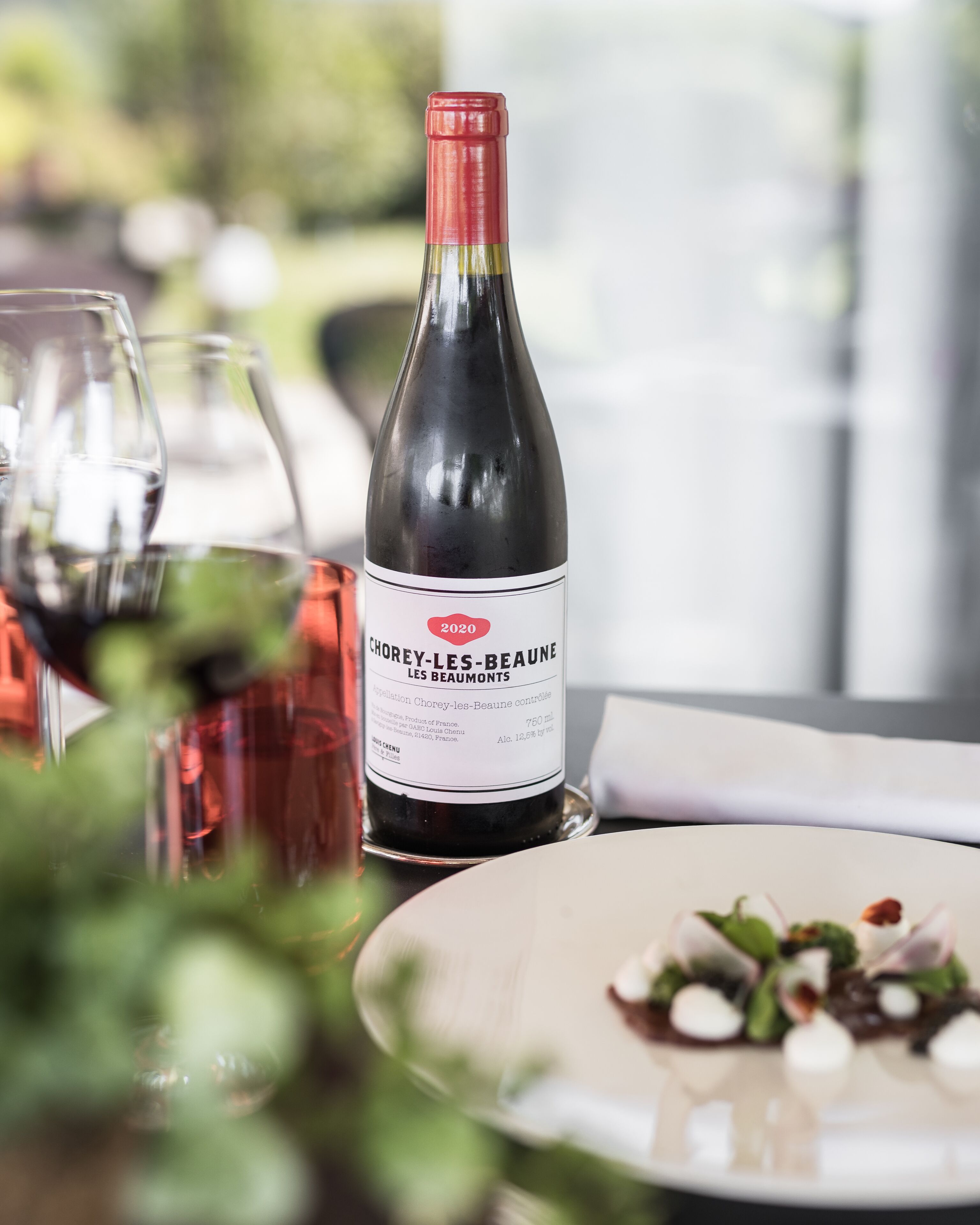 Uma garrafa de vinho Chorey-les-Beaune sobre uma mesa com copos e um prato de comida.