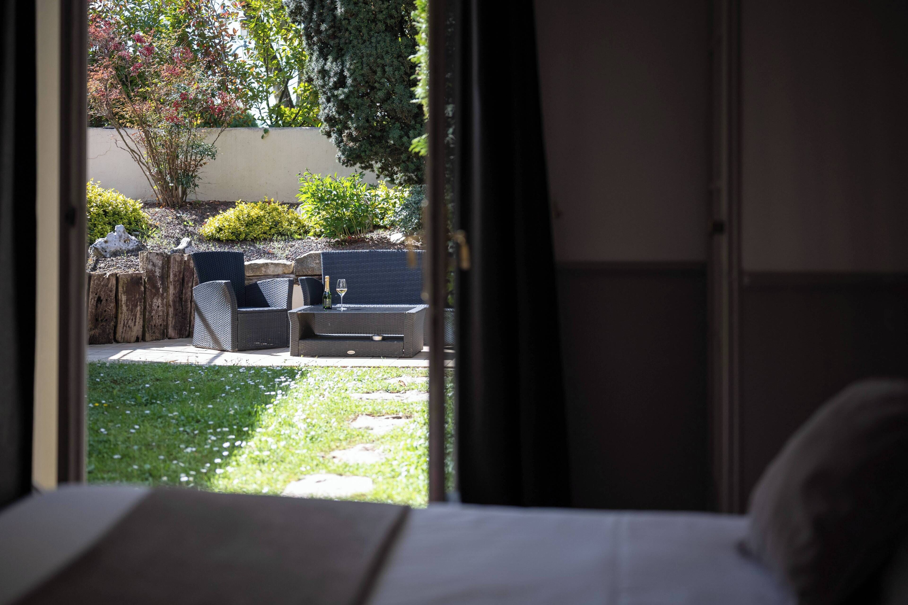 Una habitación con cama, ventana y vista a un área de estar exterior con sillas y una mesa.