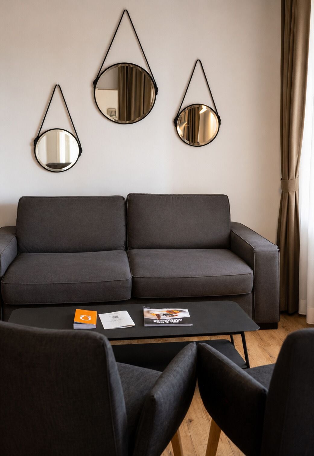En moderne stue med en grå sofa, et sofabord og tre spejle på væggen.