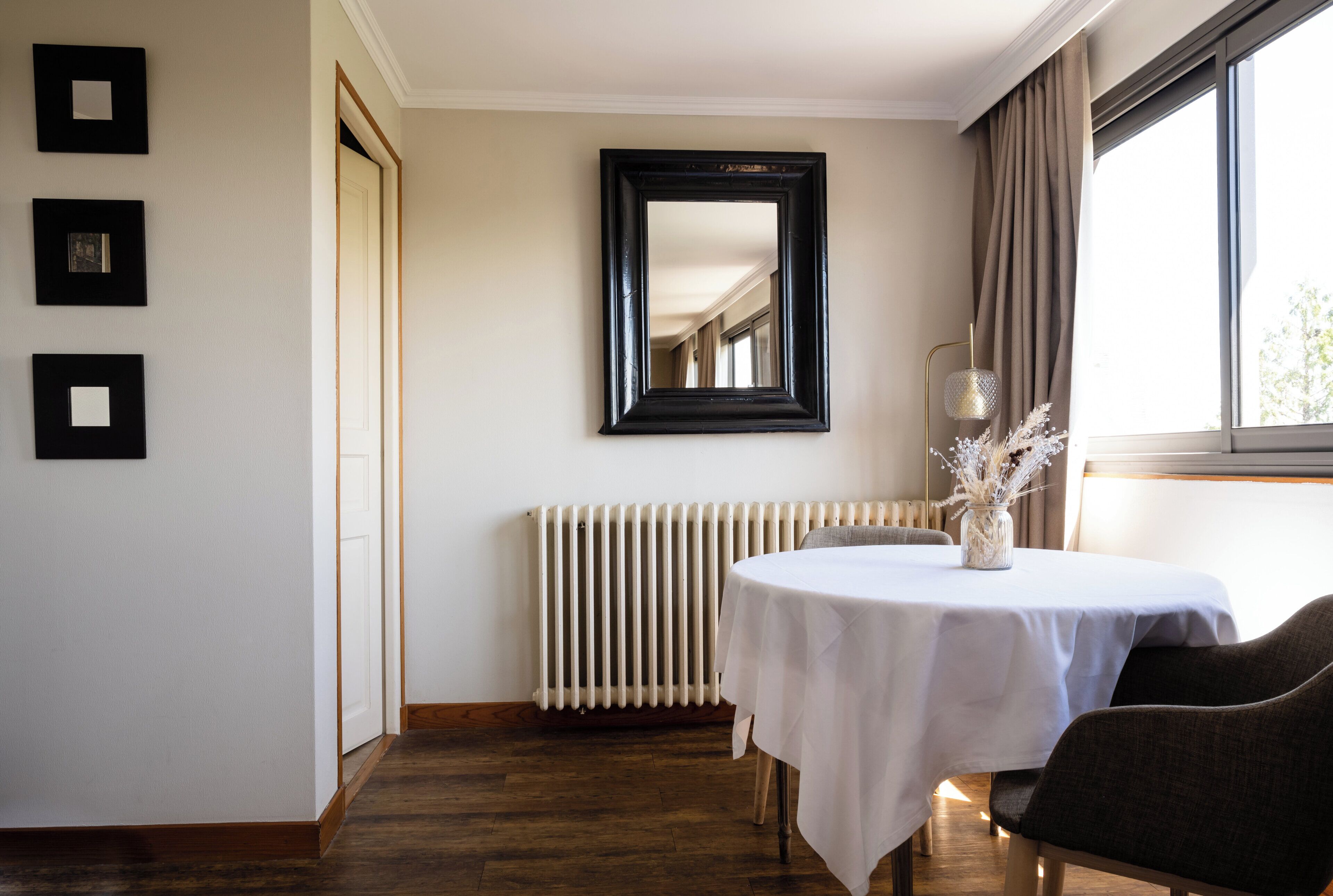 A room with a white table, a chair, a radiator, and a window with curtains.