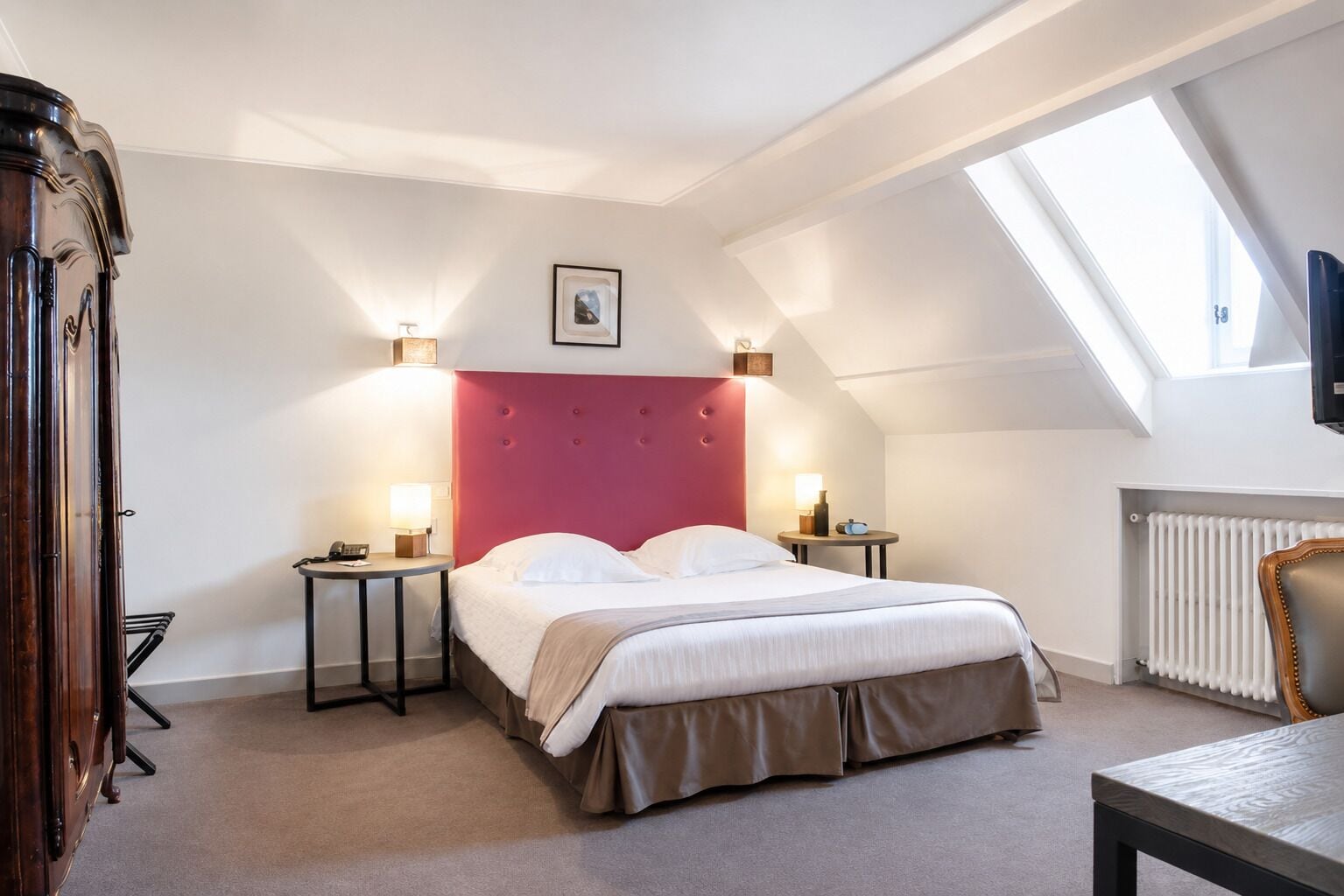 A bedroom with a bed, bedside tables, a dresser, a radiator, and a skylight.